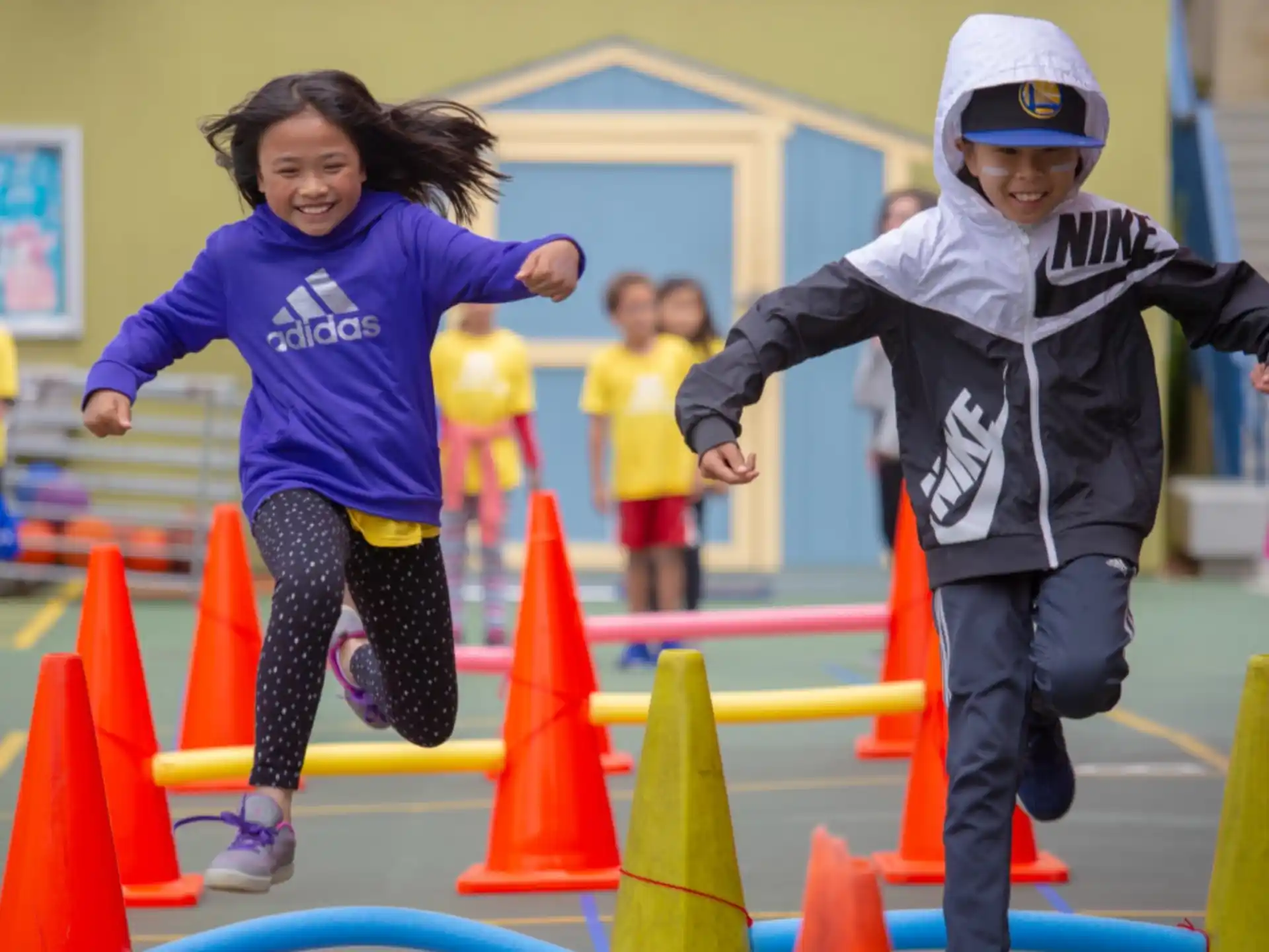 a couple of kids running on a track with orange cones