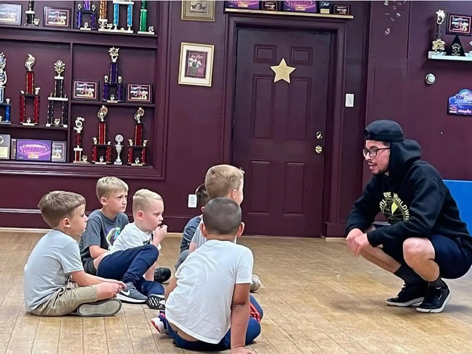 a person kneeling down with a group of boys sitting on the floor