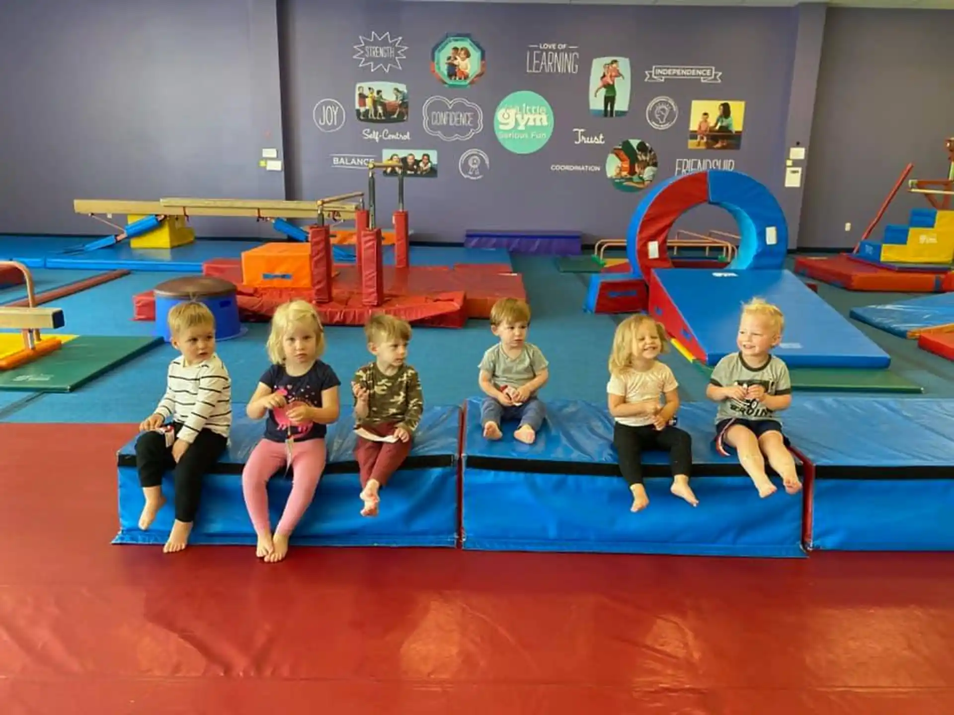a group of children sitting on a blue mat in front of a screen