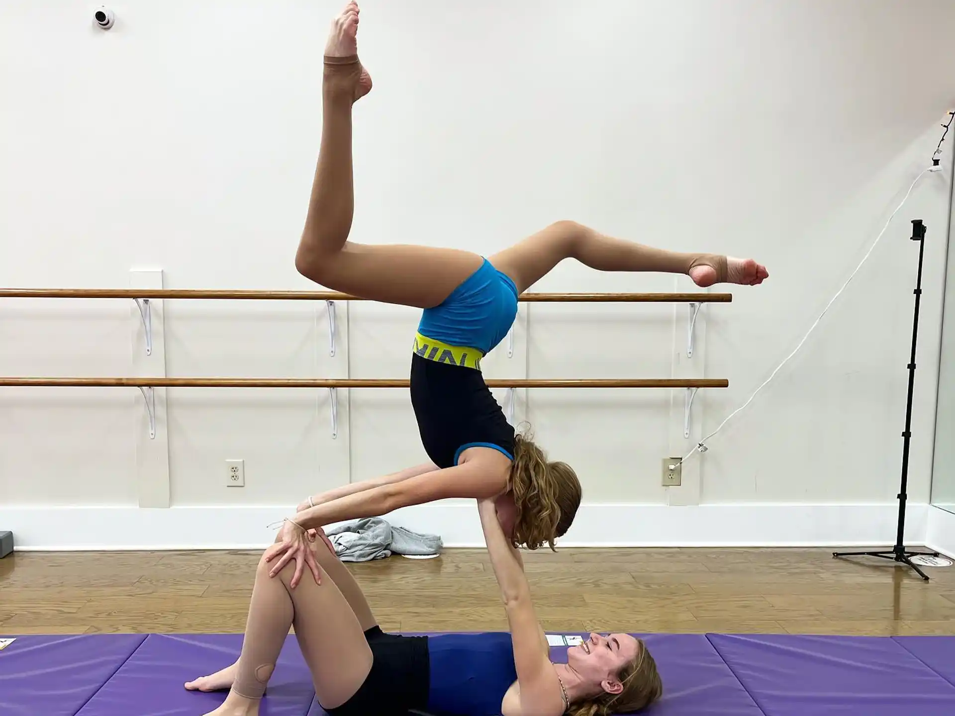 a woman doing a handstand on a mat with another woman lying on her back