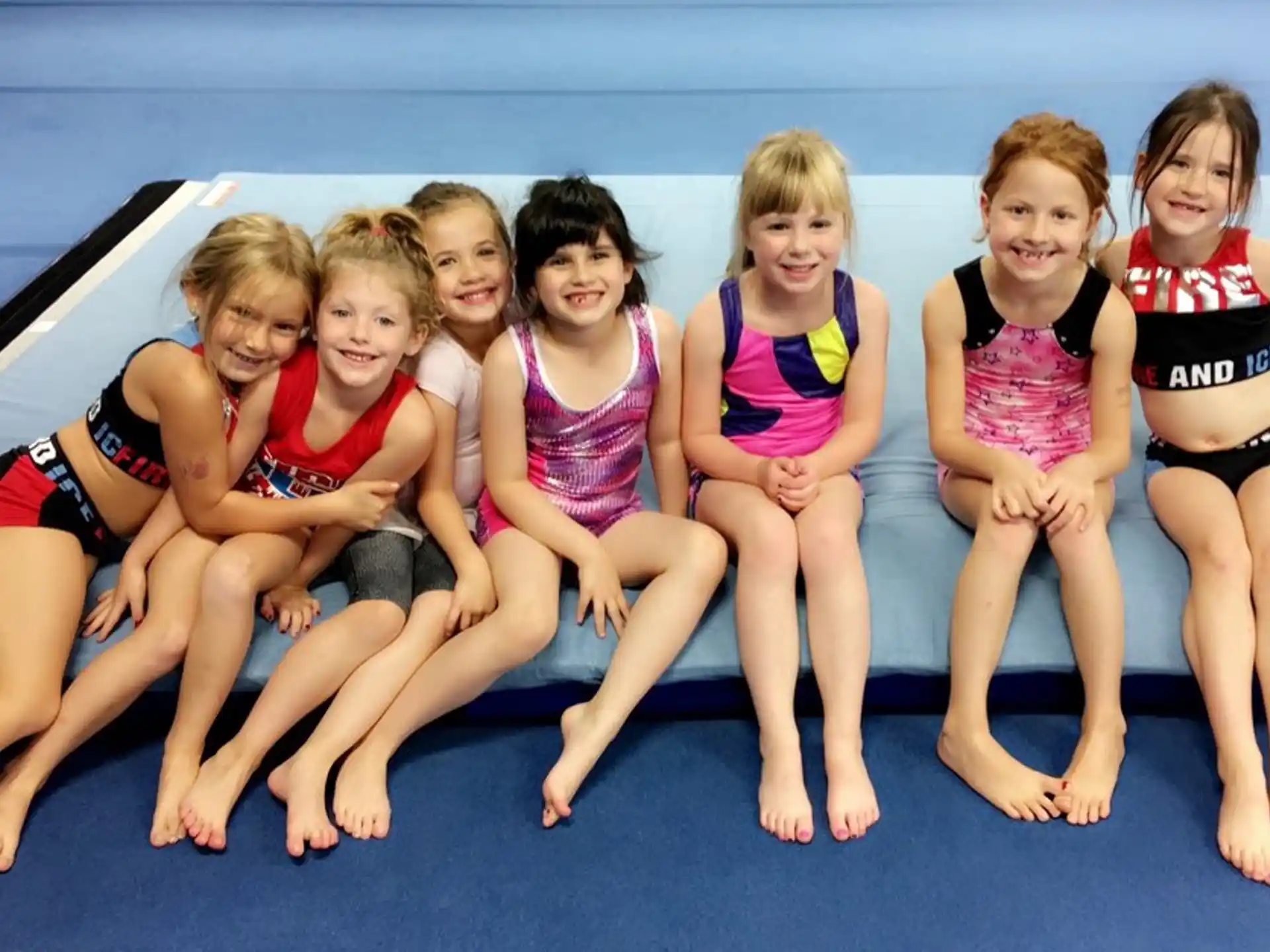 a group of girls in swimsuits sitting on a blue mat
