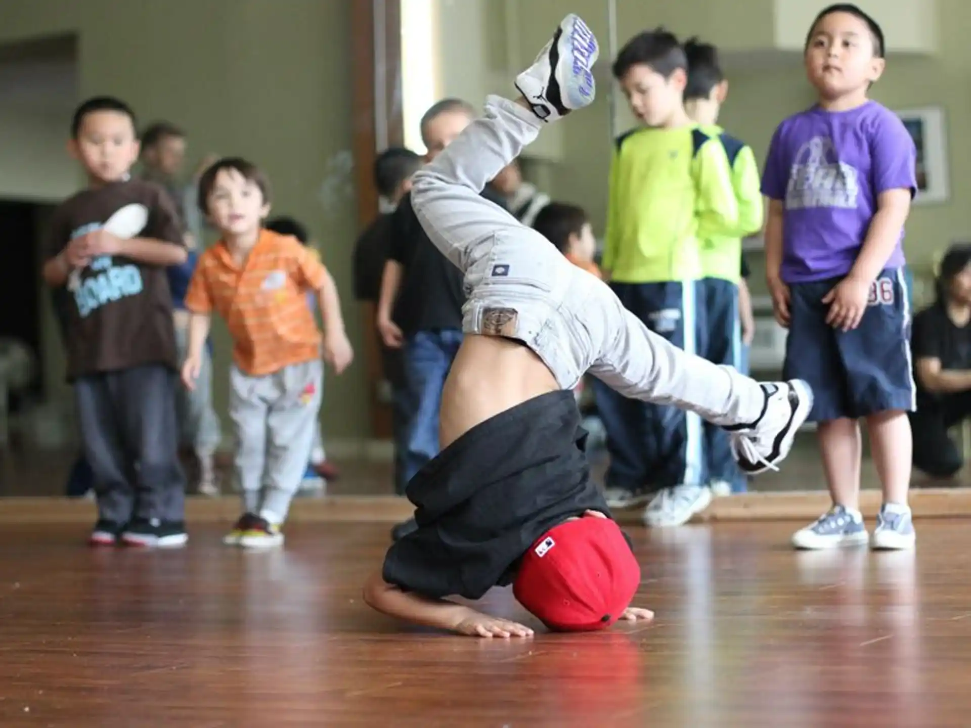 a person doing a handstand on a wood floor with other kids