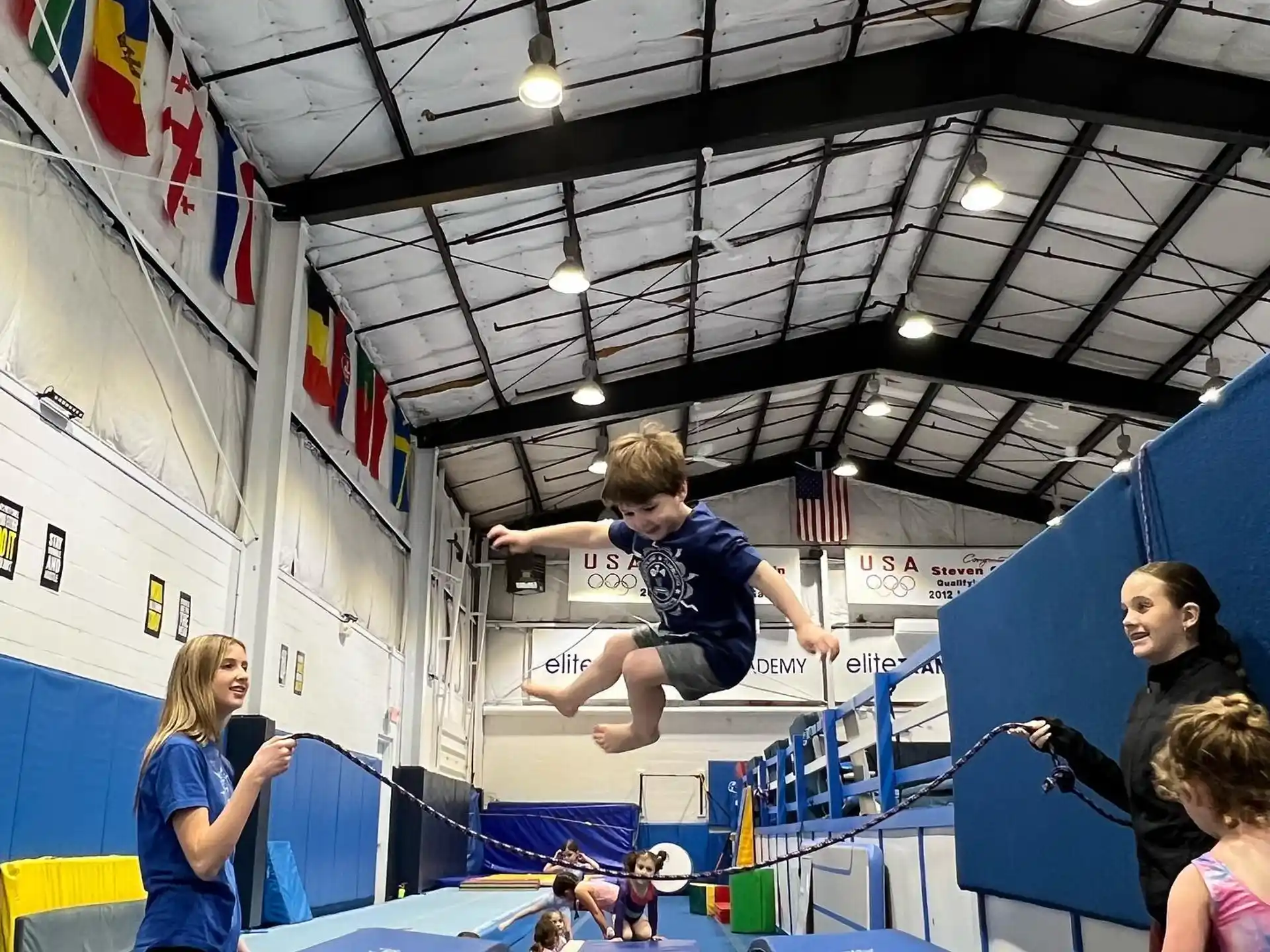 a boy jumping on a trampoline in a room with people
