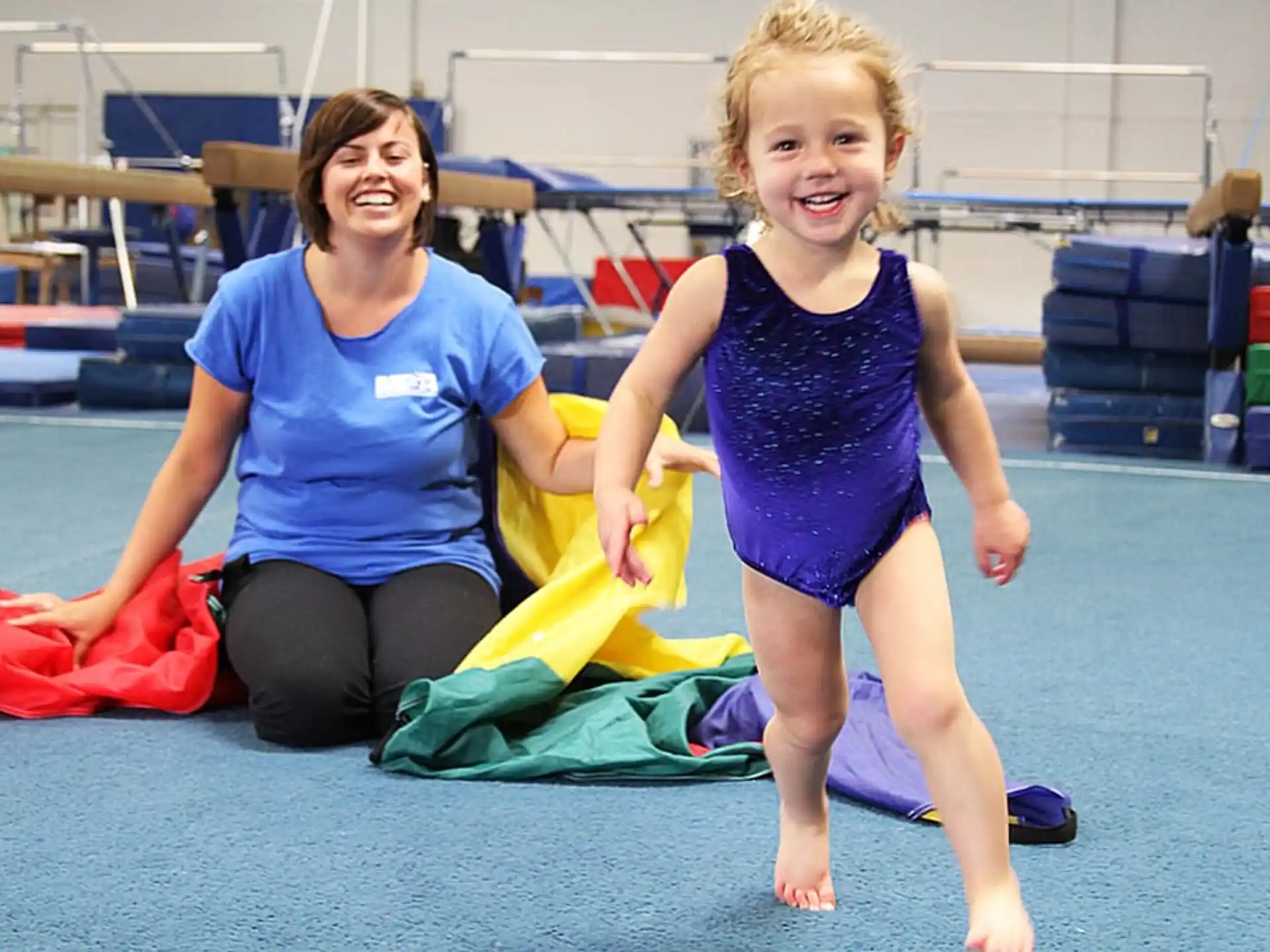 a woman and a girl on a mat in a gym