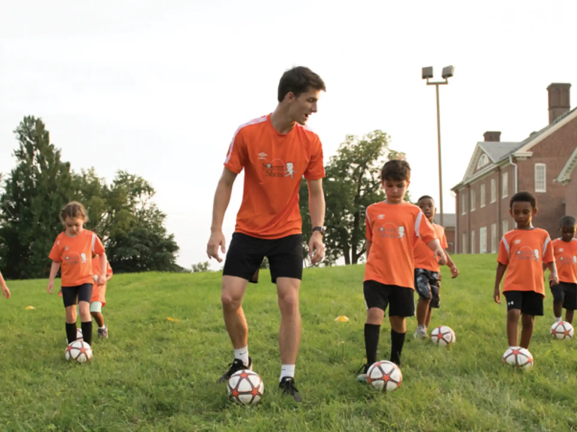 a person in orange shirt playing football with a group of kids