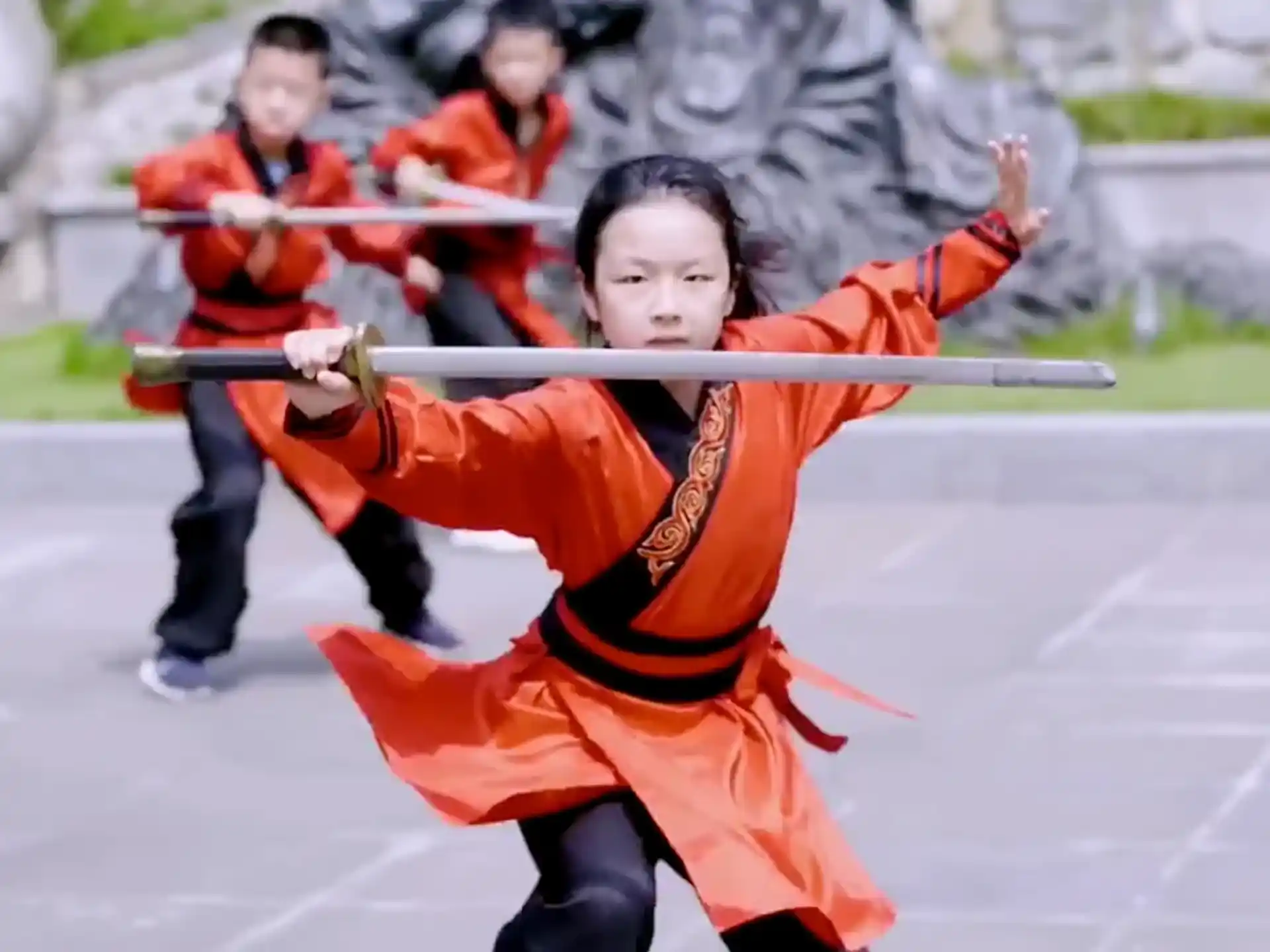 a young boy in an orange uniform holding a sword