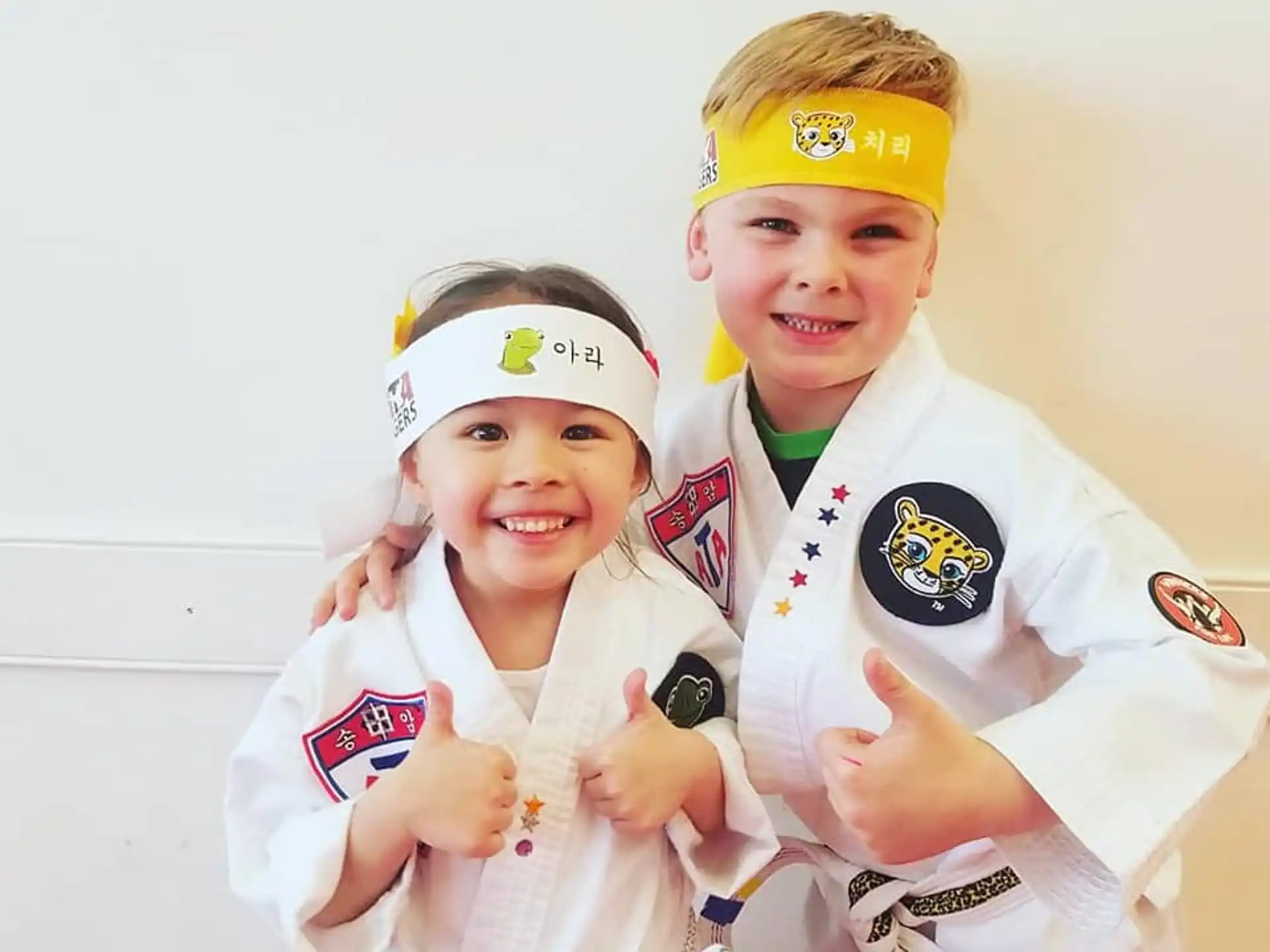 a couple of kids wearing white uniforms and holding up their hands