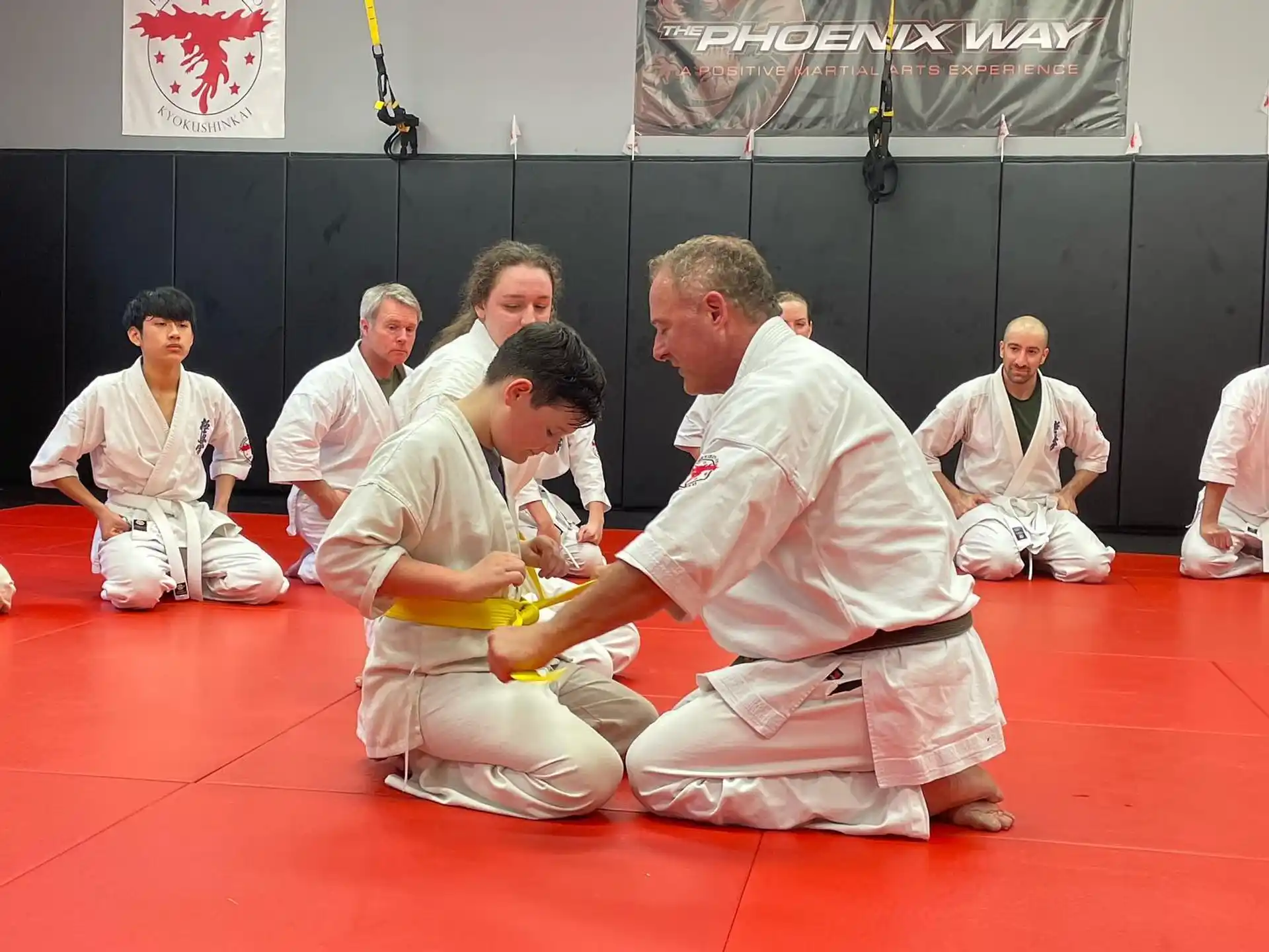 a group of men in white karate uniforms kneeling on a red mat