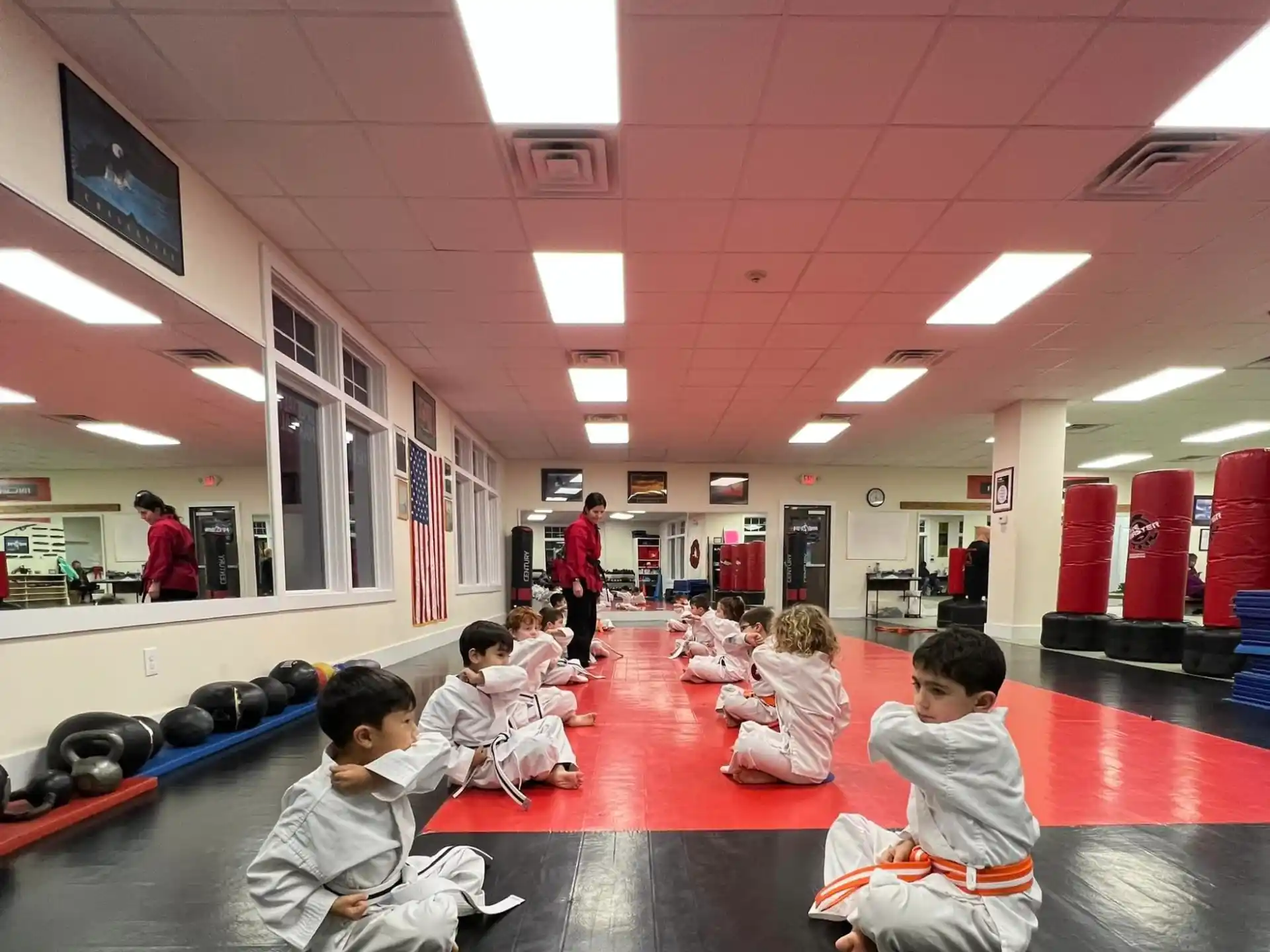 a group of children sitting on the floor in a room with a person standing and a person standing