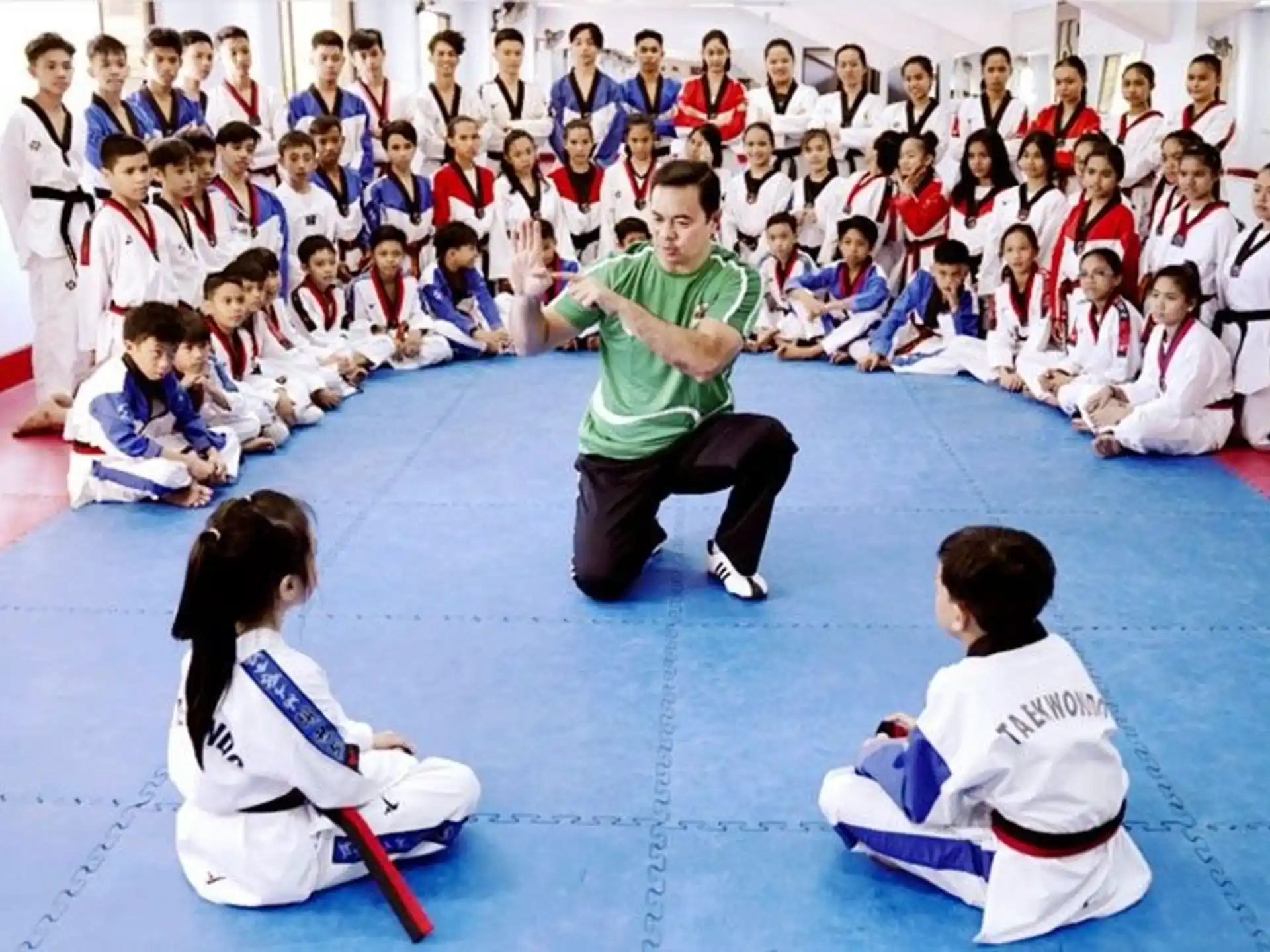 a person kneeling in front of a group of children in karate uniforms