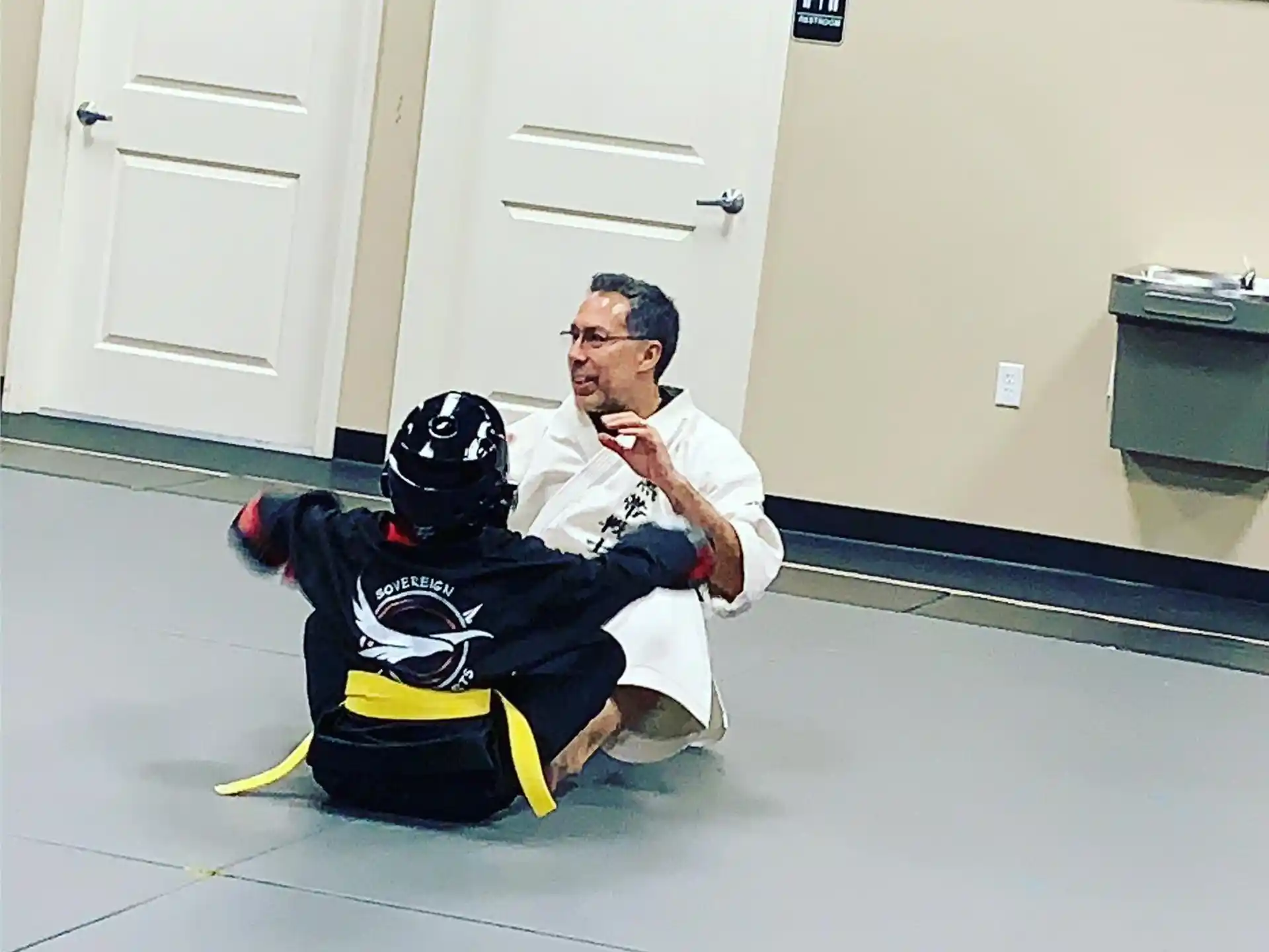 a man in a white shirt and black helmet kneeling next to a man in a white suit