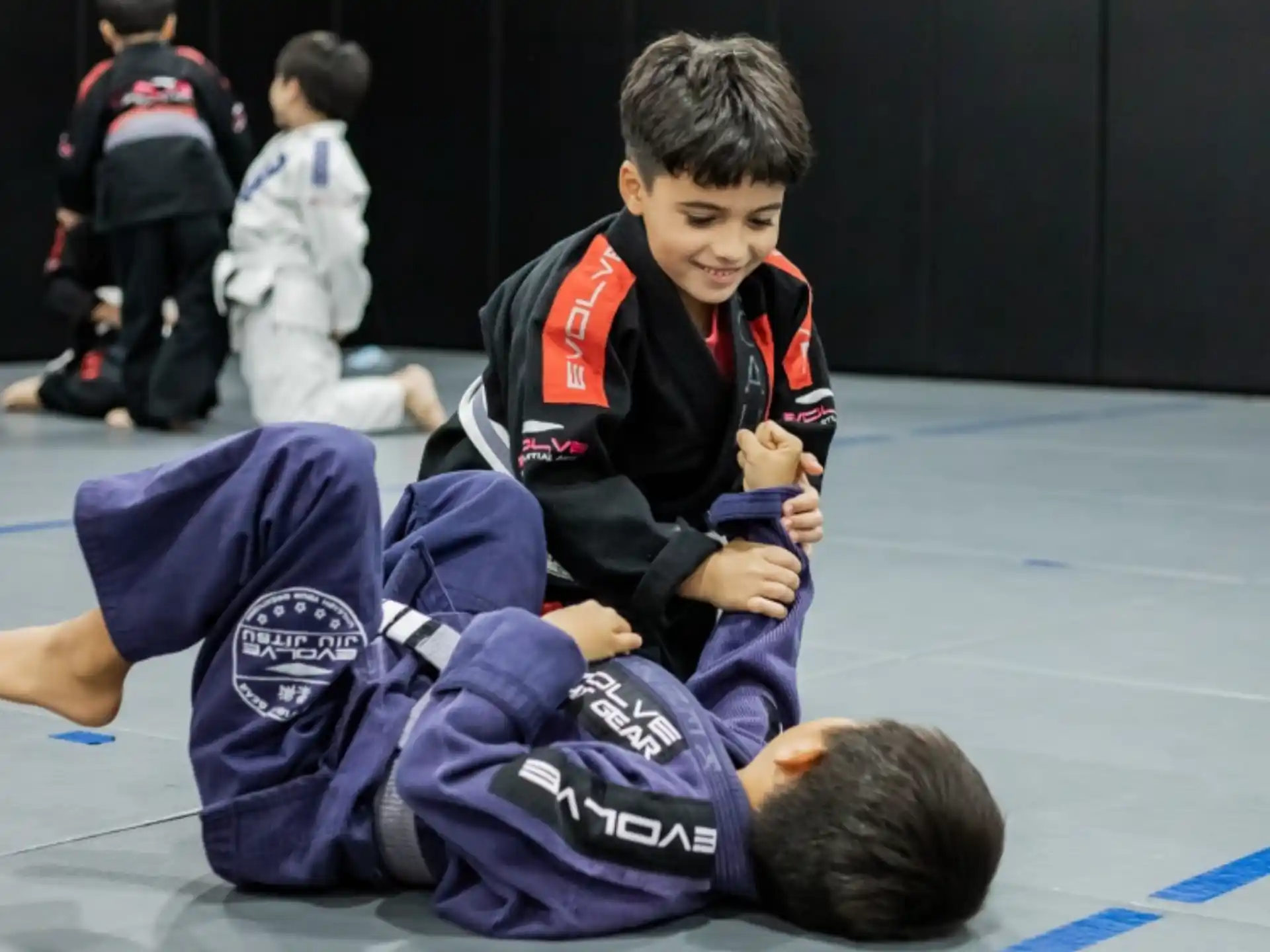 a boy in a uniform kneeling on the ground with another boy in the back