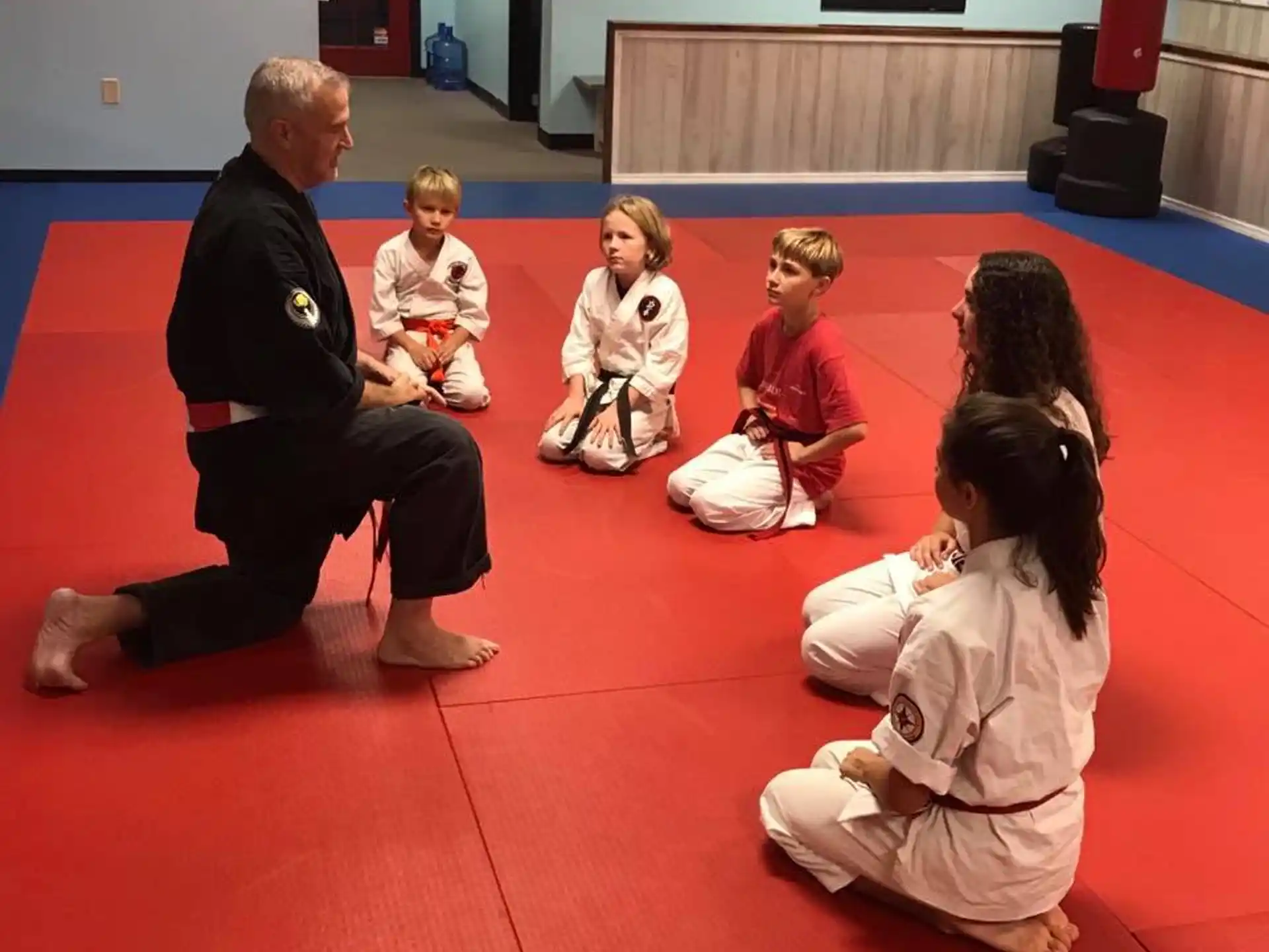 a person kneeling down to a group of children sitting on the floor