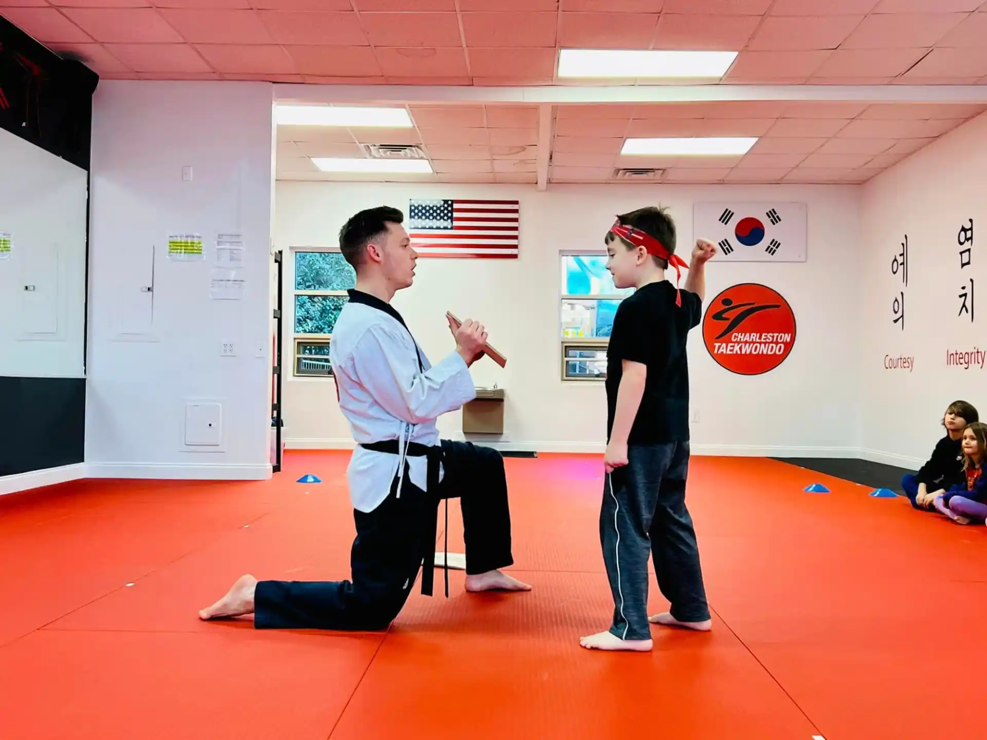 a person kneeling on the floor next to a boy in a karate uniform