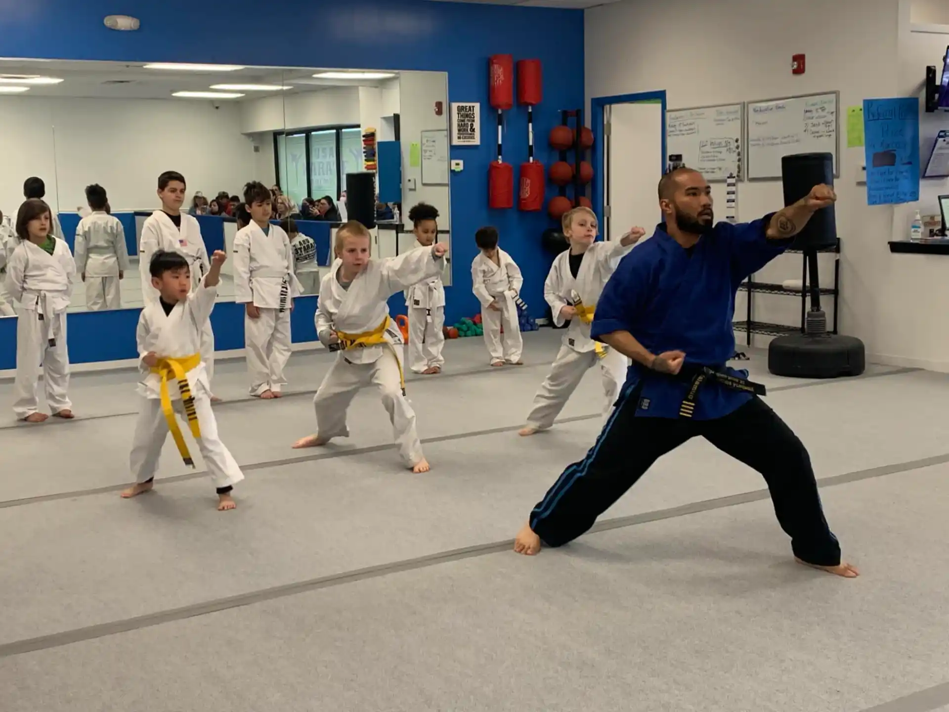 a person in a karate uniform with a group of children in a room