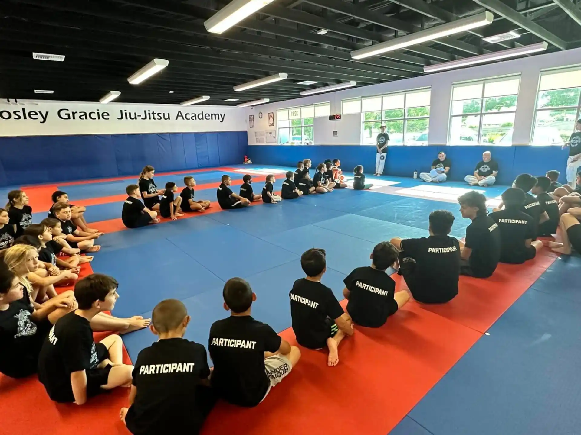 a group of people sitting on a red mat in a room with a person standing on a stage
