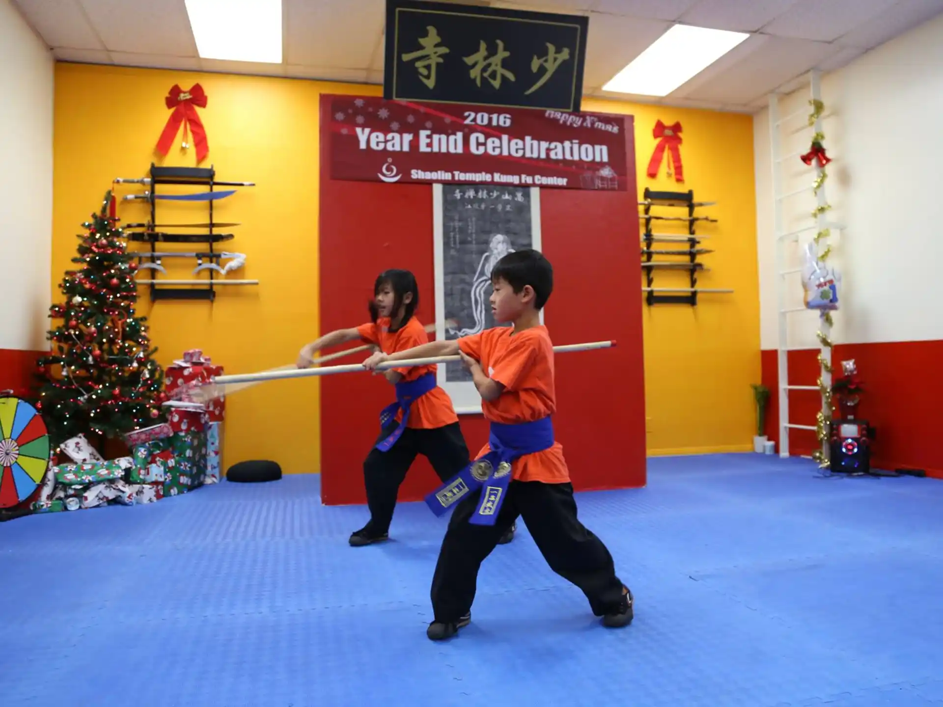 a couple of kids playing with a sword in a room with a christmas tree