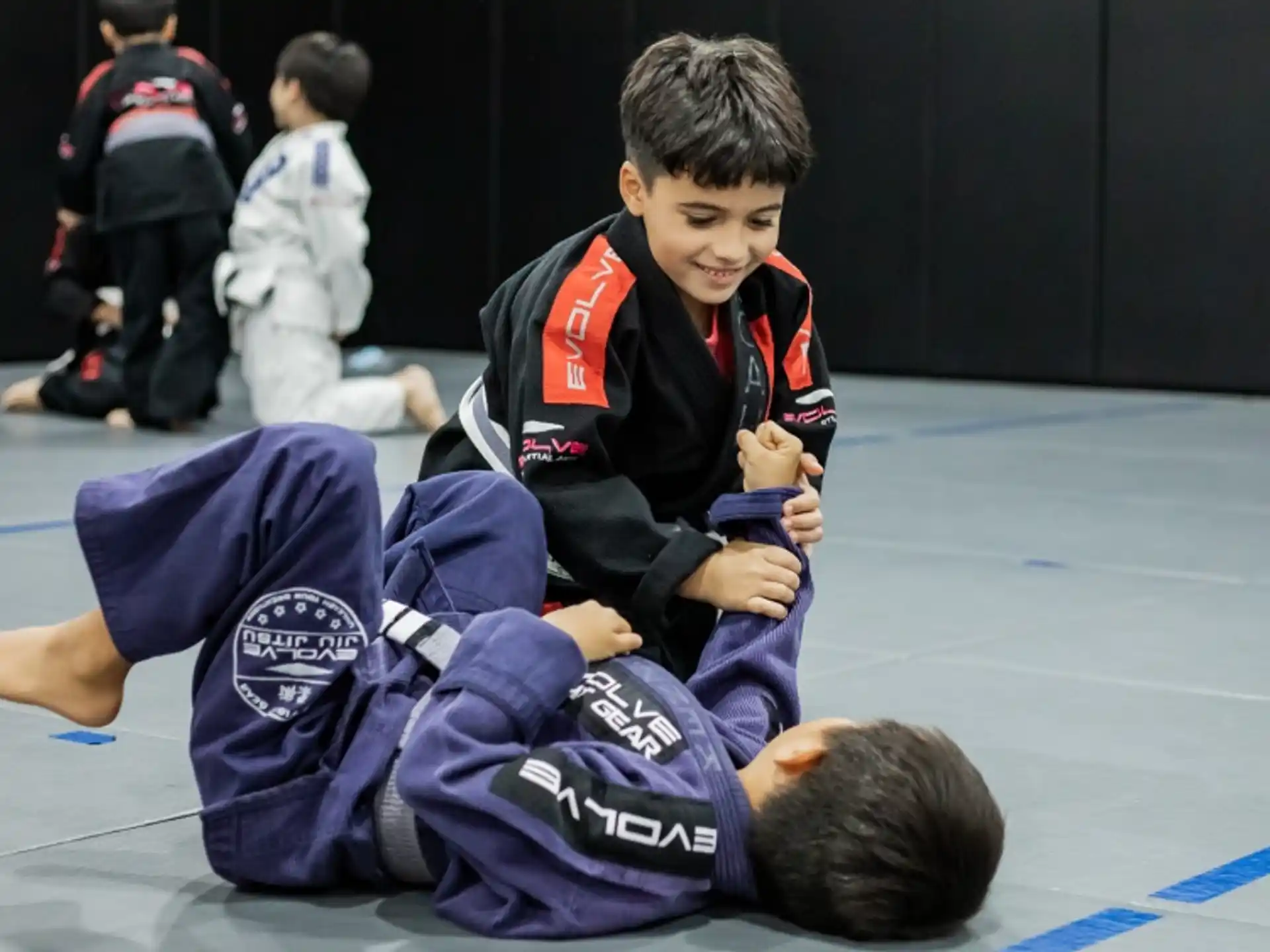 a boy in a uniform kneeling on the ground with another boy in the back