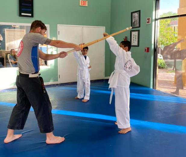 a person in a karate uniform holding a stick in front of a person in a white shirt