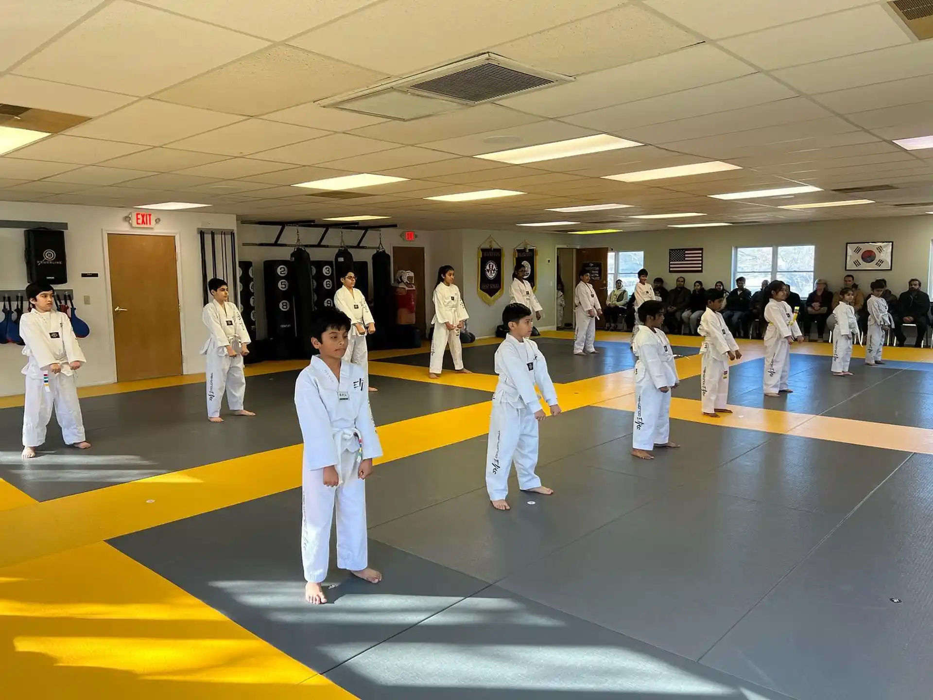 a group of people in white karate uniforms in a room with a yellow floor and a wood floor
