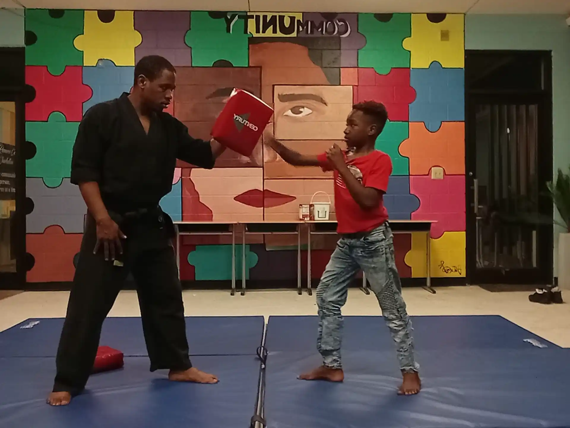 a man and a boy holding red objects in a room with a wall with art on it