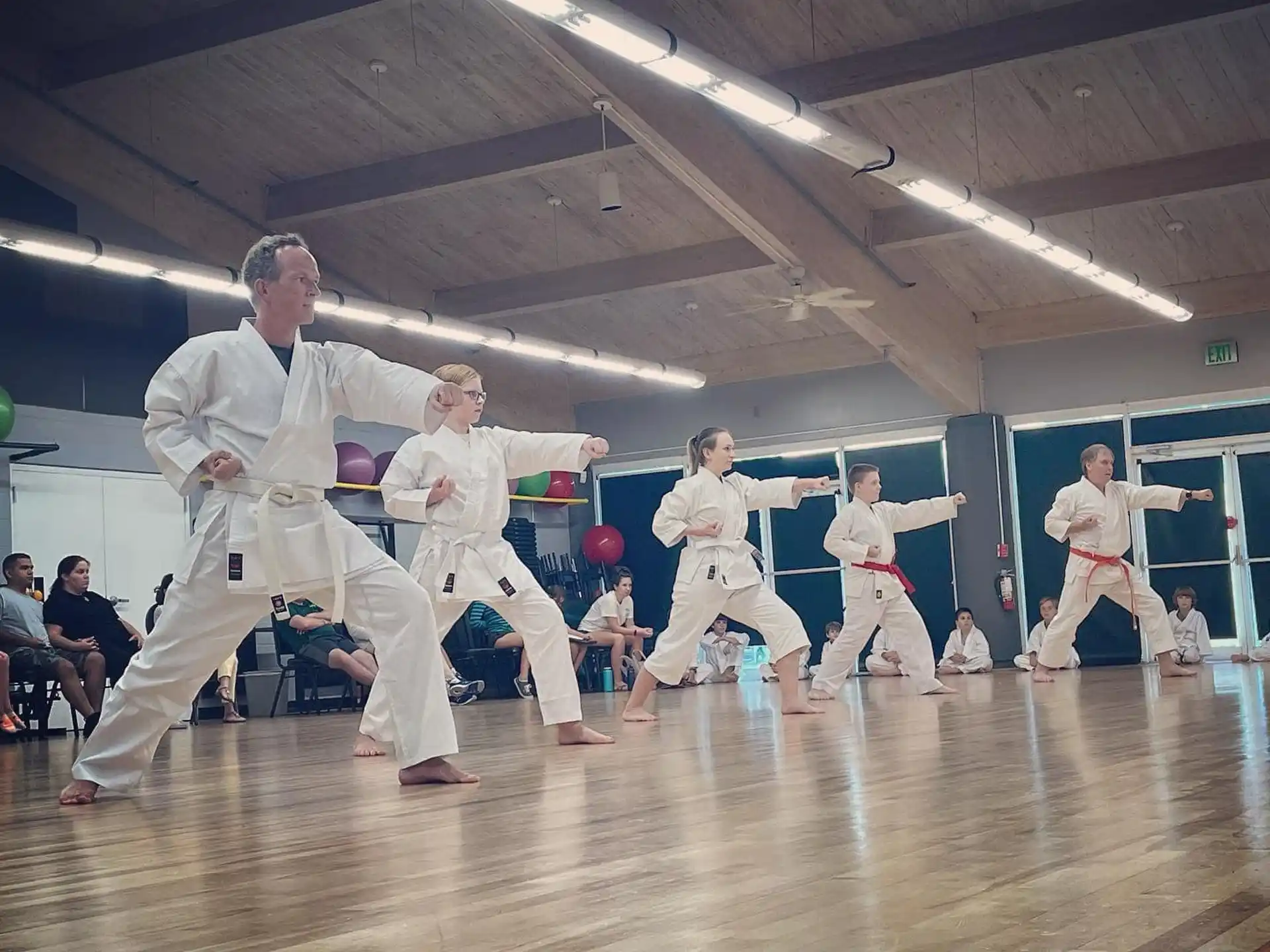 a group of people in white karate uniforms in a room with a wood floor and a wood floor