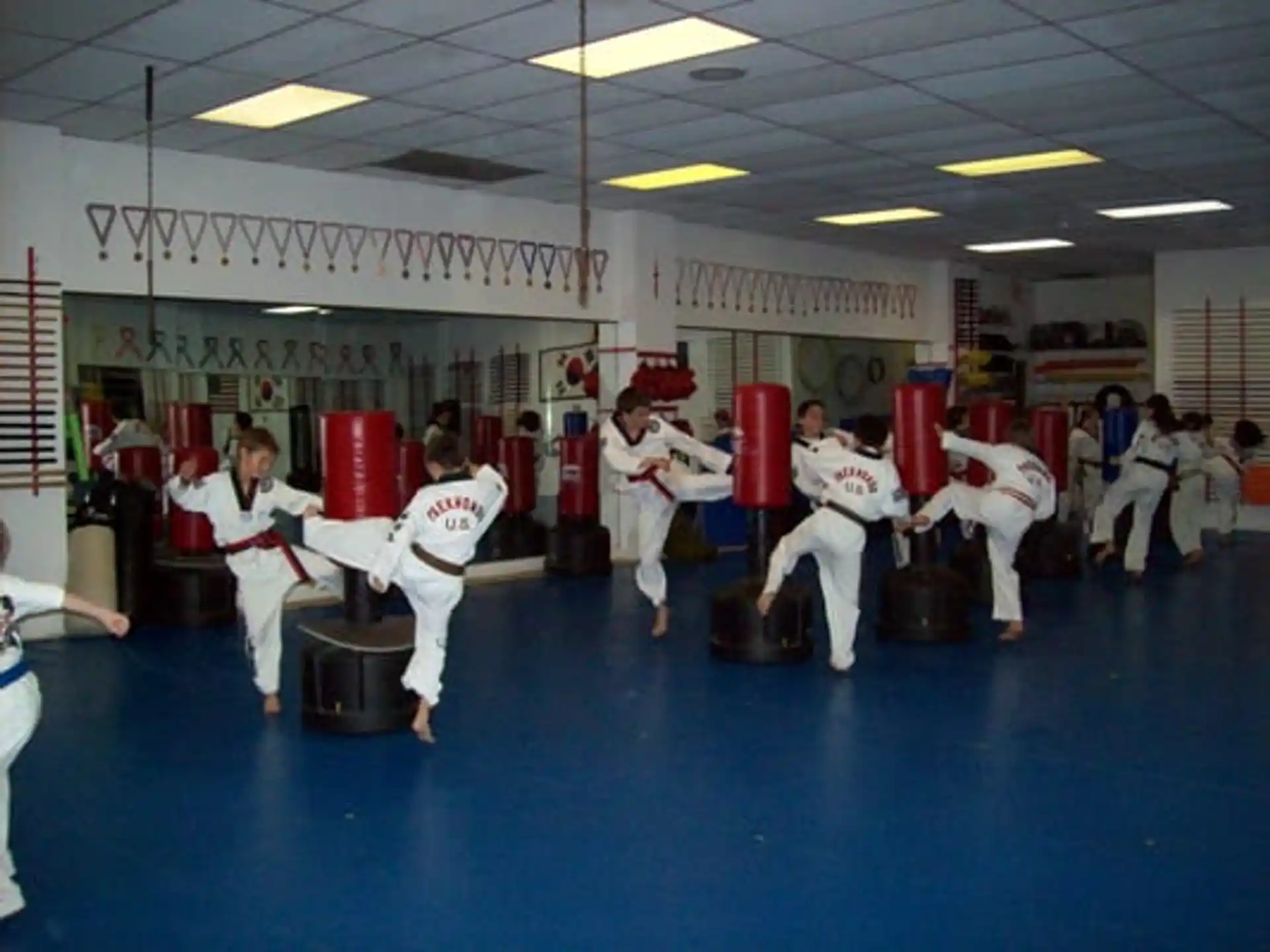 a group of people in white karate uniforms in a room with a blue mat and a red punching