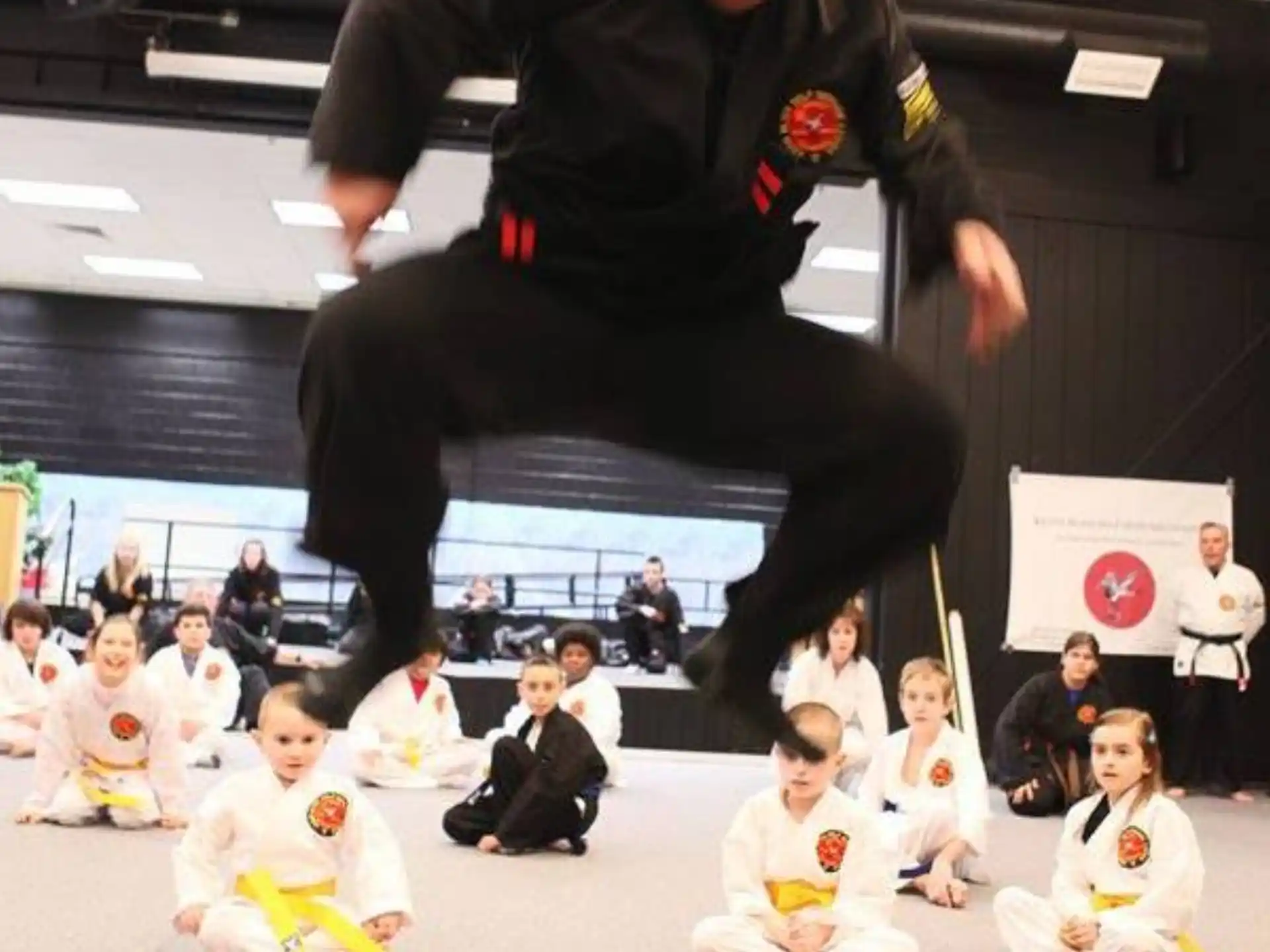 a man in black suit doing a karate move with a group of children