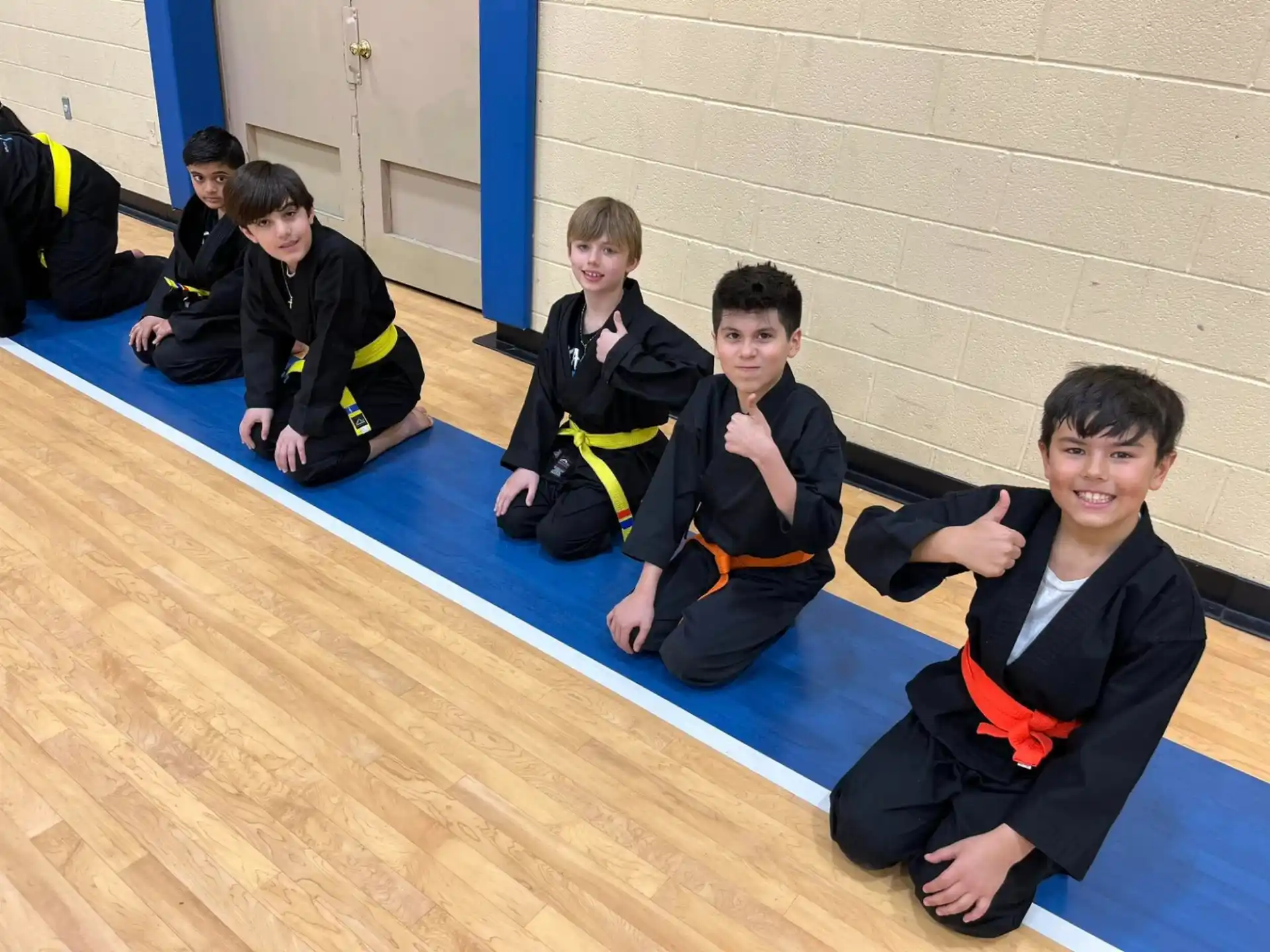 a group of boys in black and orange uniforms sitting on the floor