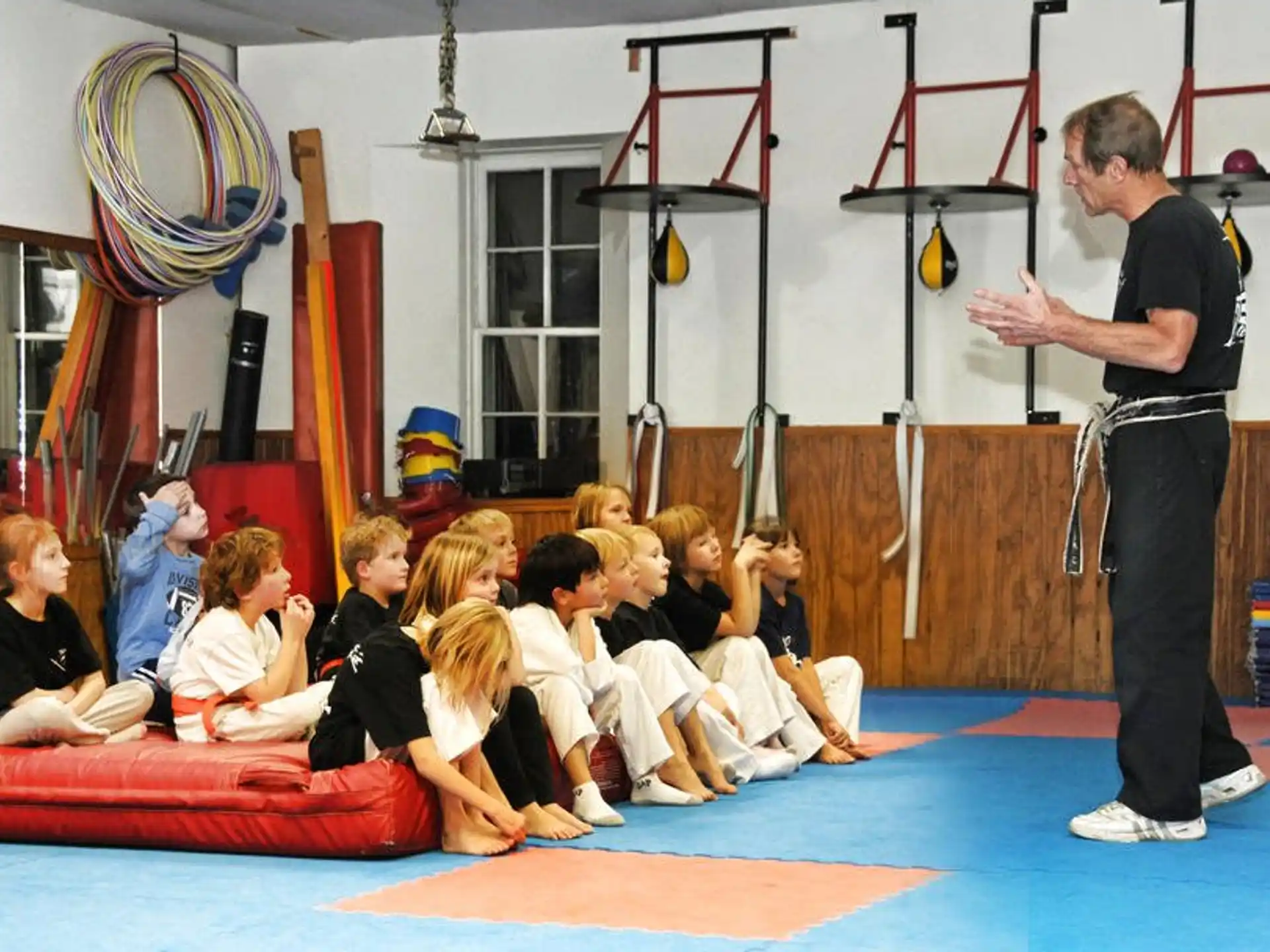 a person standing in front of a group of children sitting on a mat
