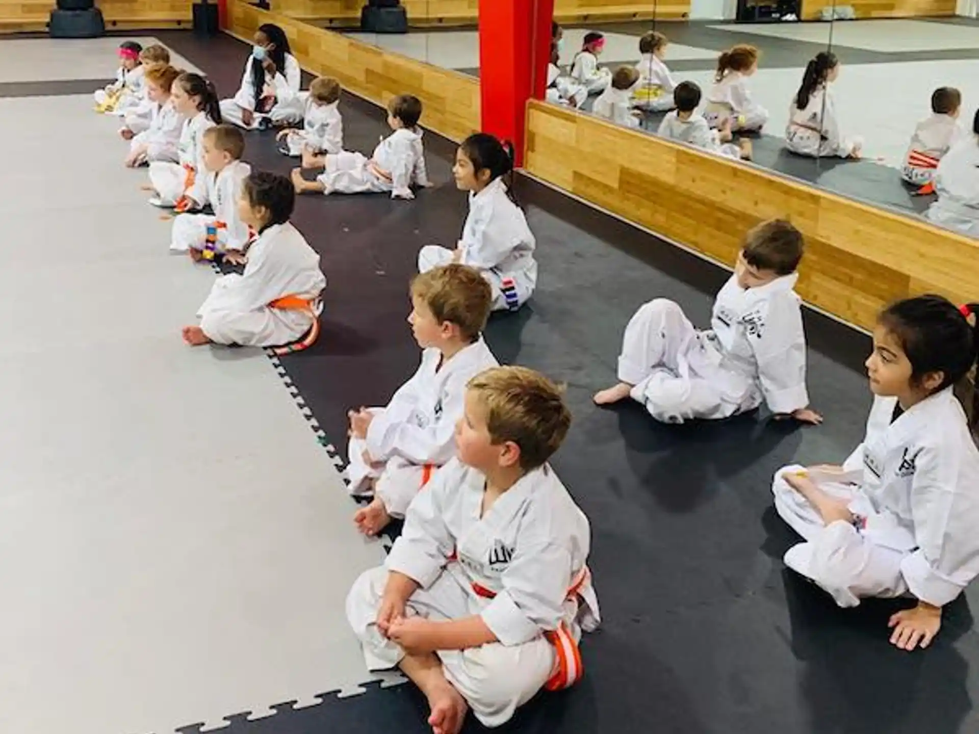 a group of children in white karate uniforms sitting on the floor