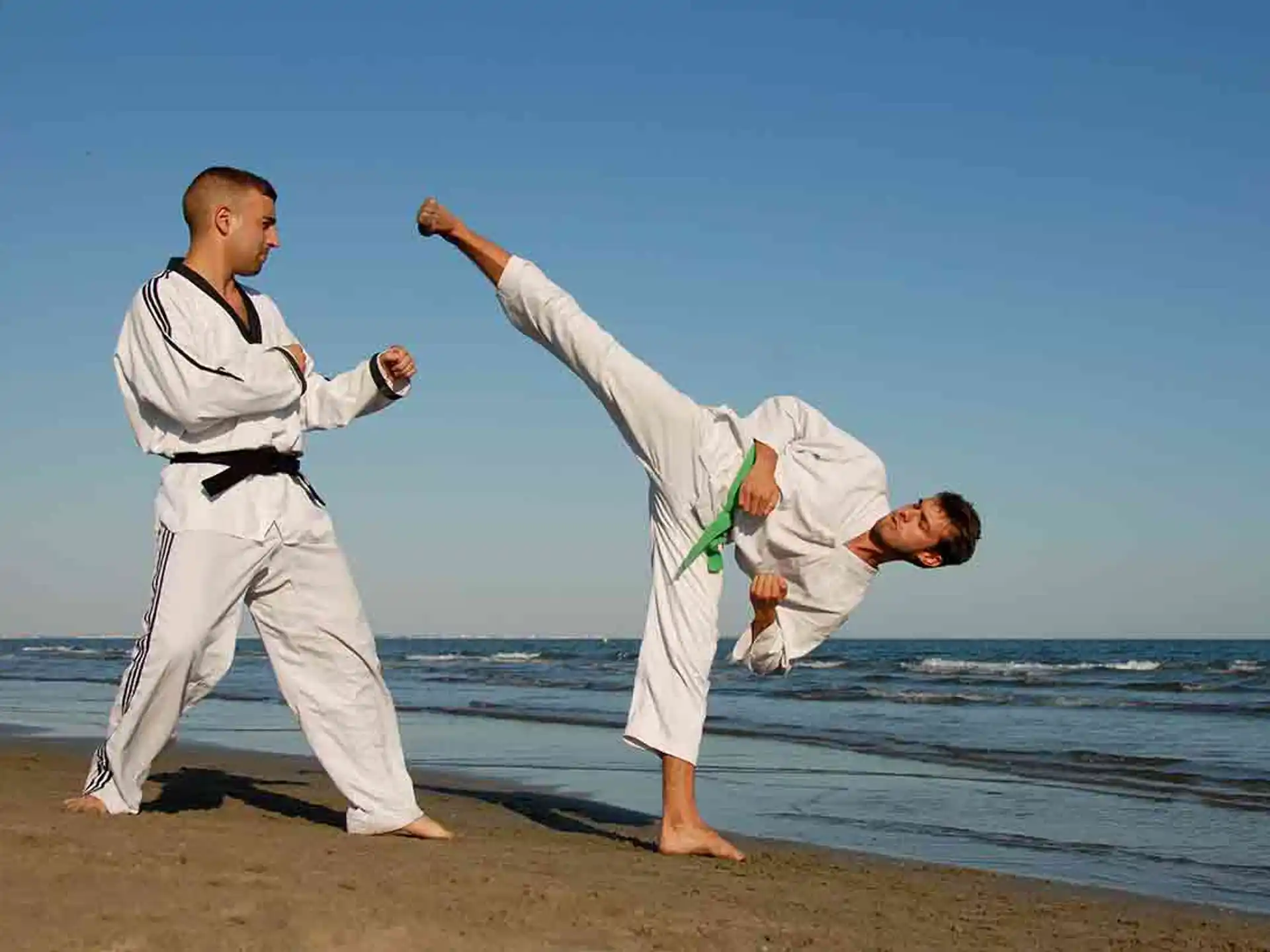 a man kicking another man in the face on a beach