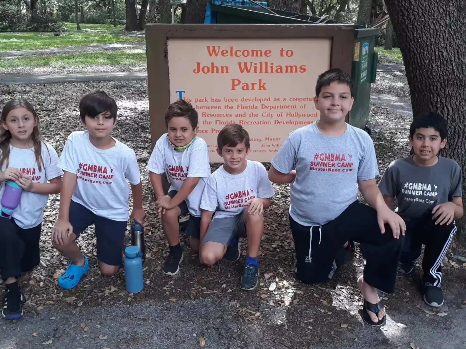a group of kids sitting on the ground in front of a sign