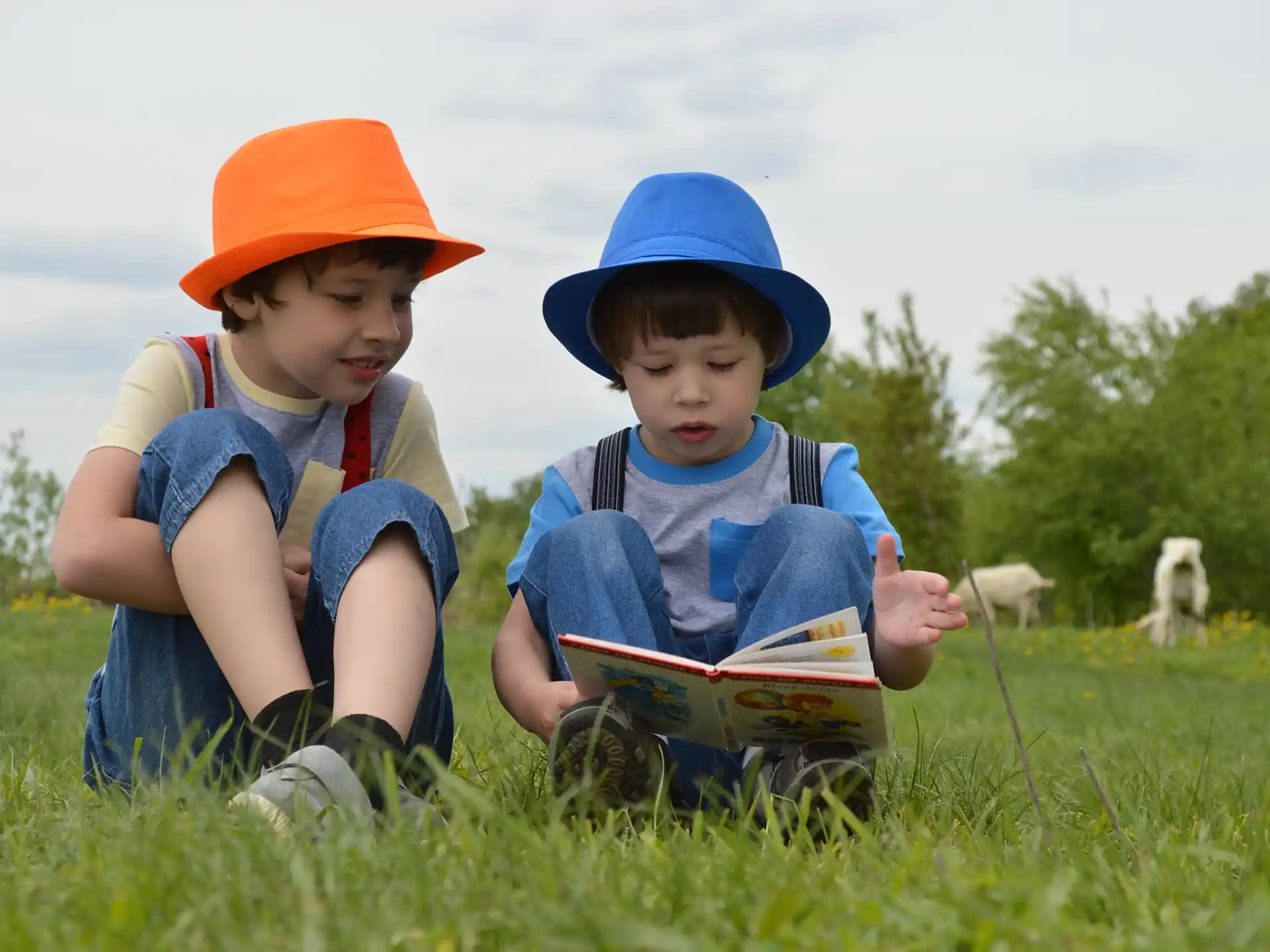 a couple of kids in hats reading a book in a field