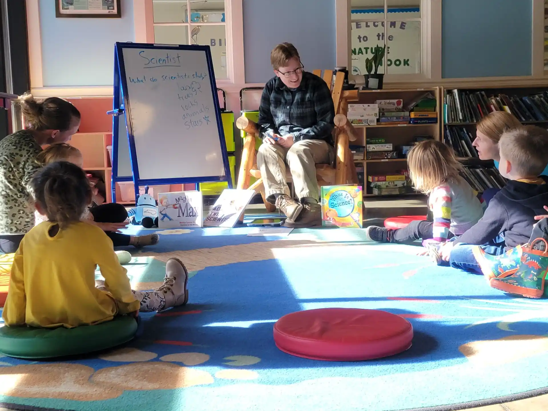 a group of children sitting on the floor in front of a whiteboard