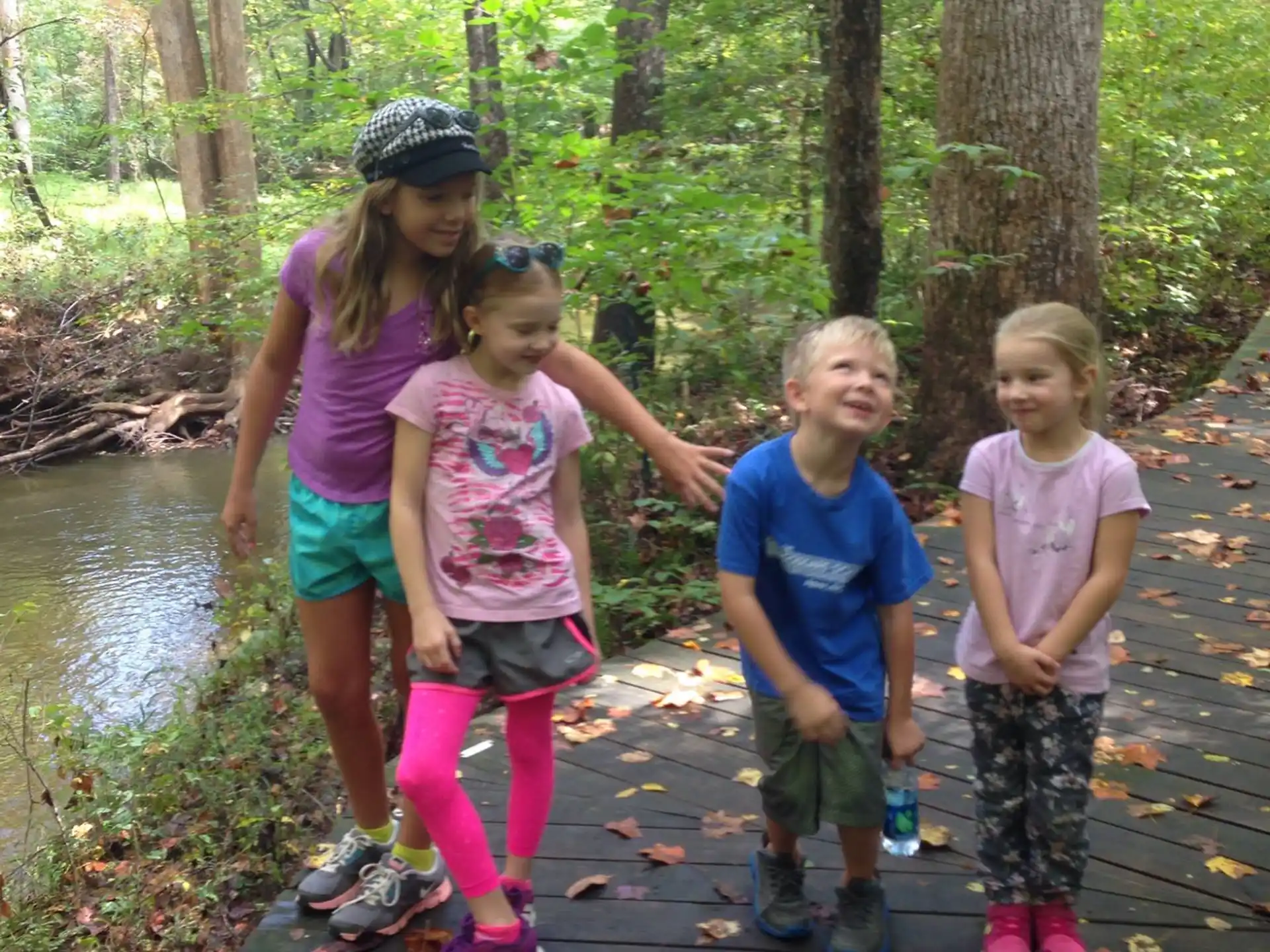 a group of children standing on a wooden bridge over a river