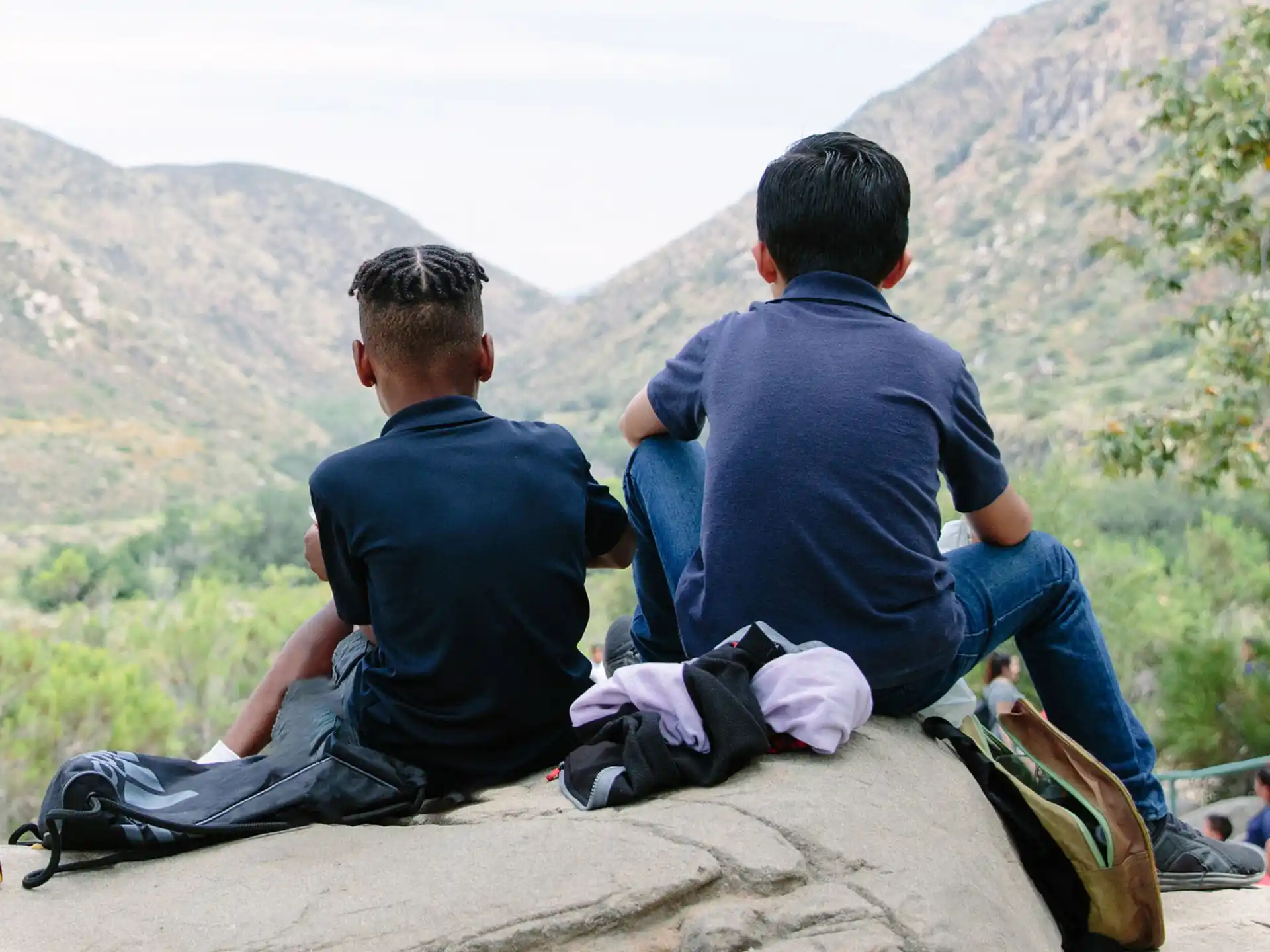 a couple of men sitting on a rock looking at a valley