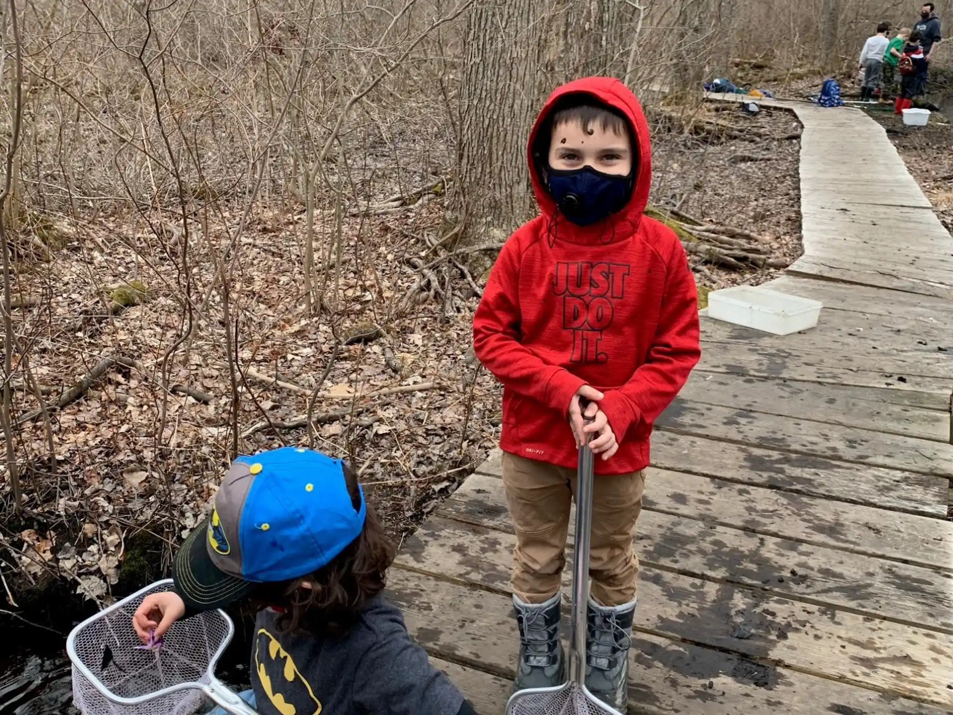 a couple of kids on a wooden bridge with a stick and a bucket