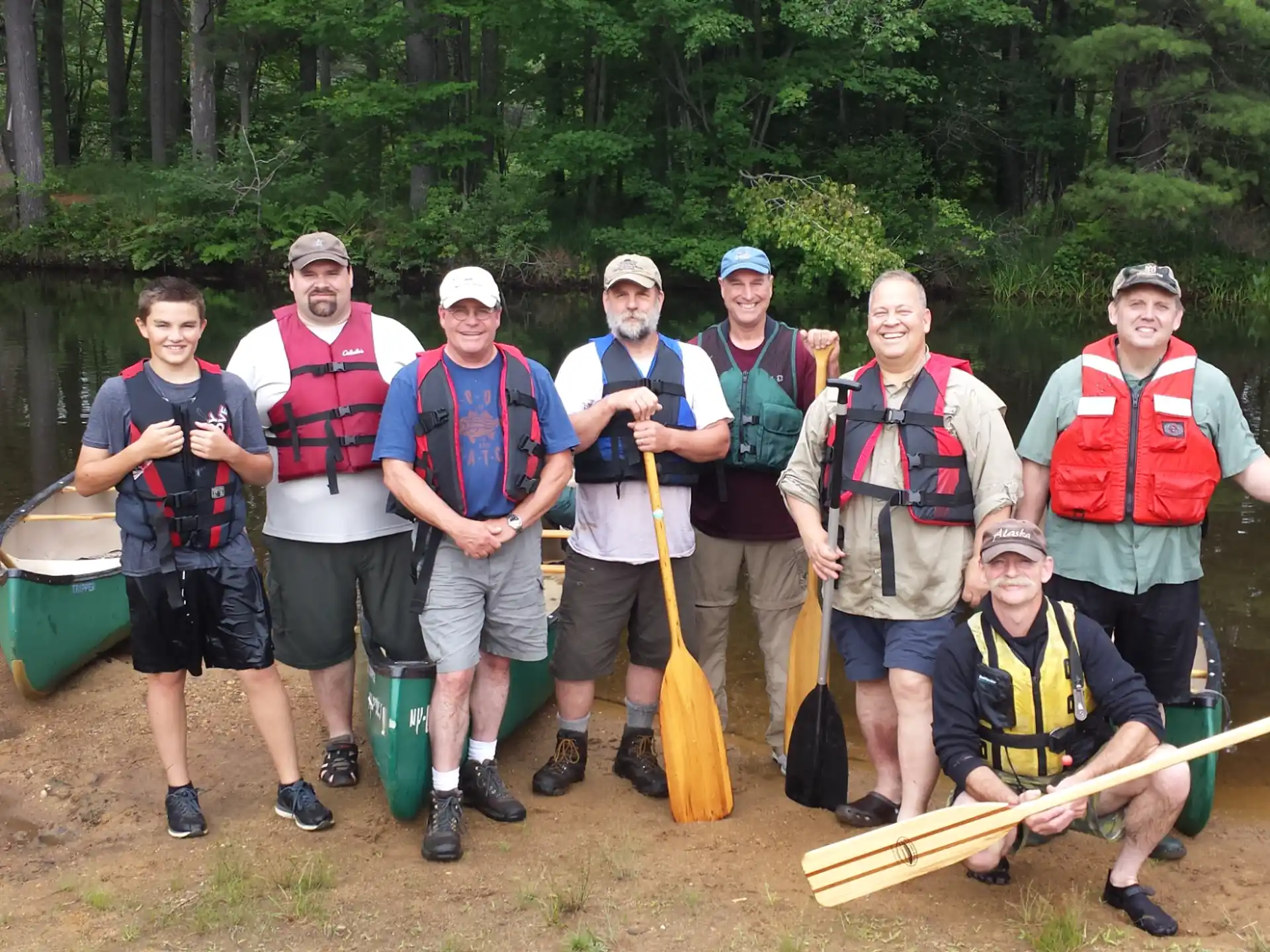 a group of men in life jackets standing in front of a lake