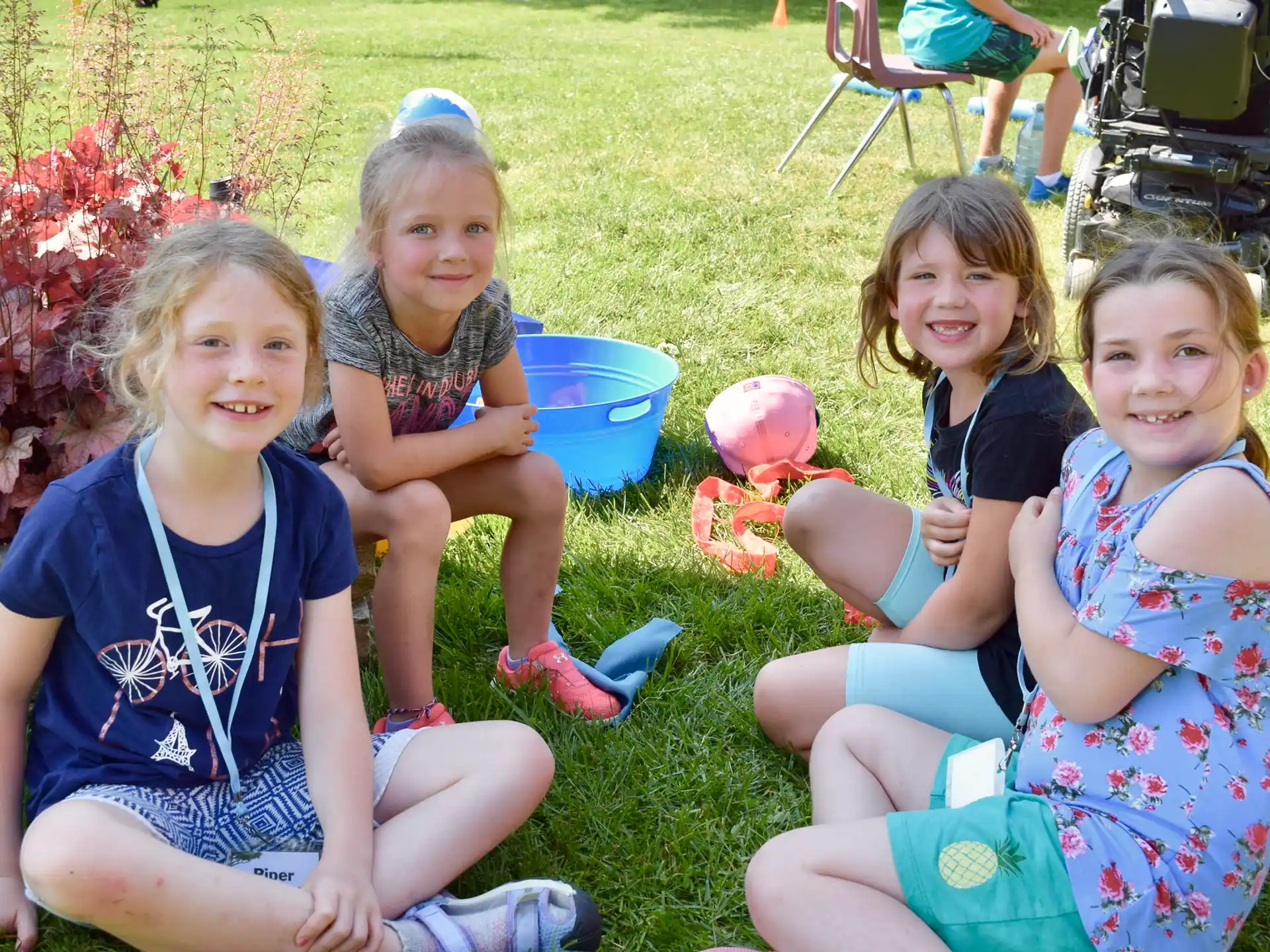 a group of girls sitting on the grass holding a bucket of candy