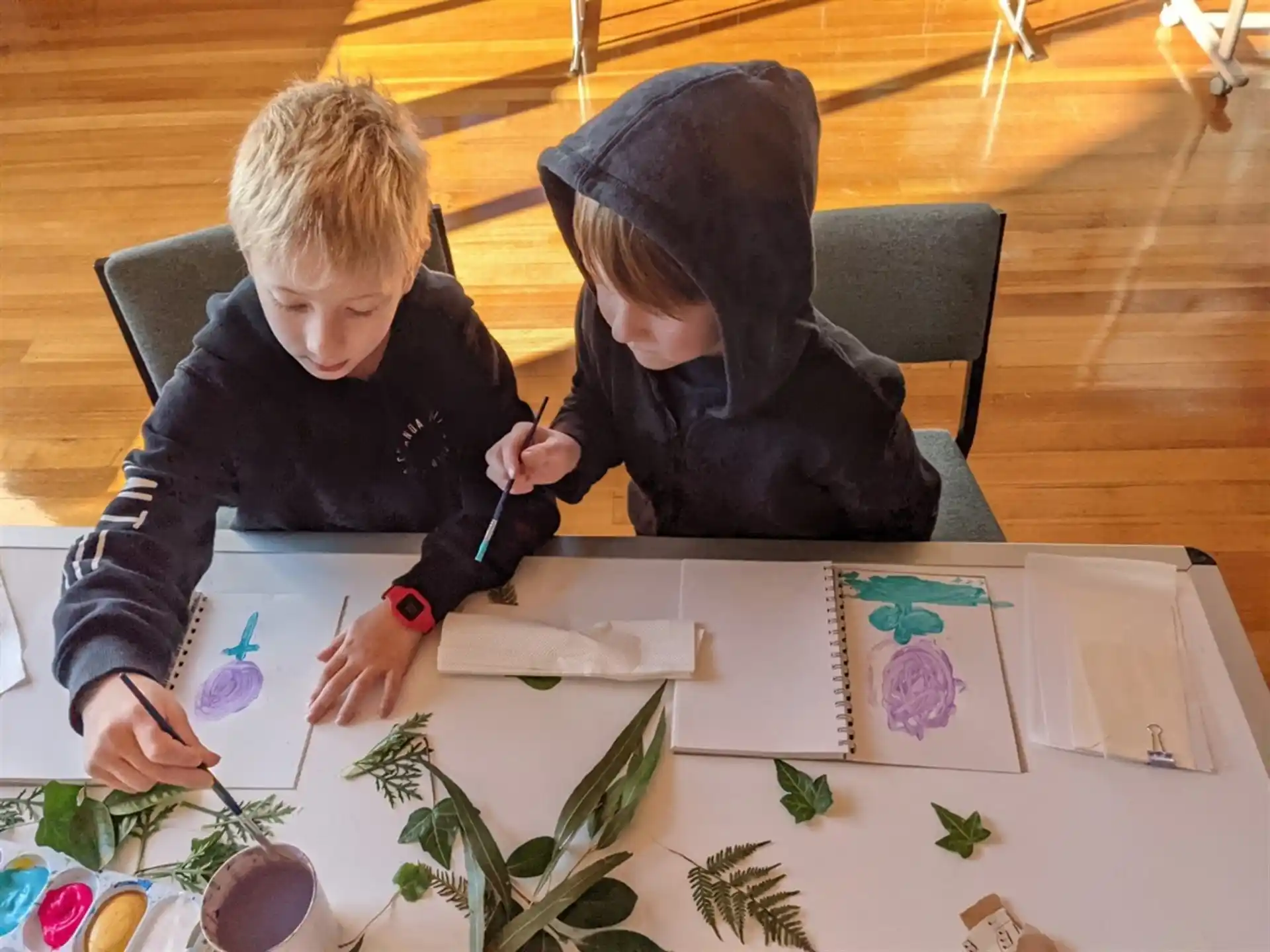 a couple of boys sitting at a table painting