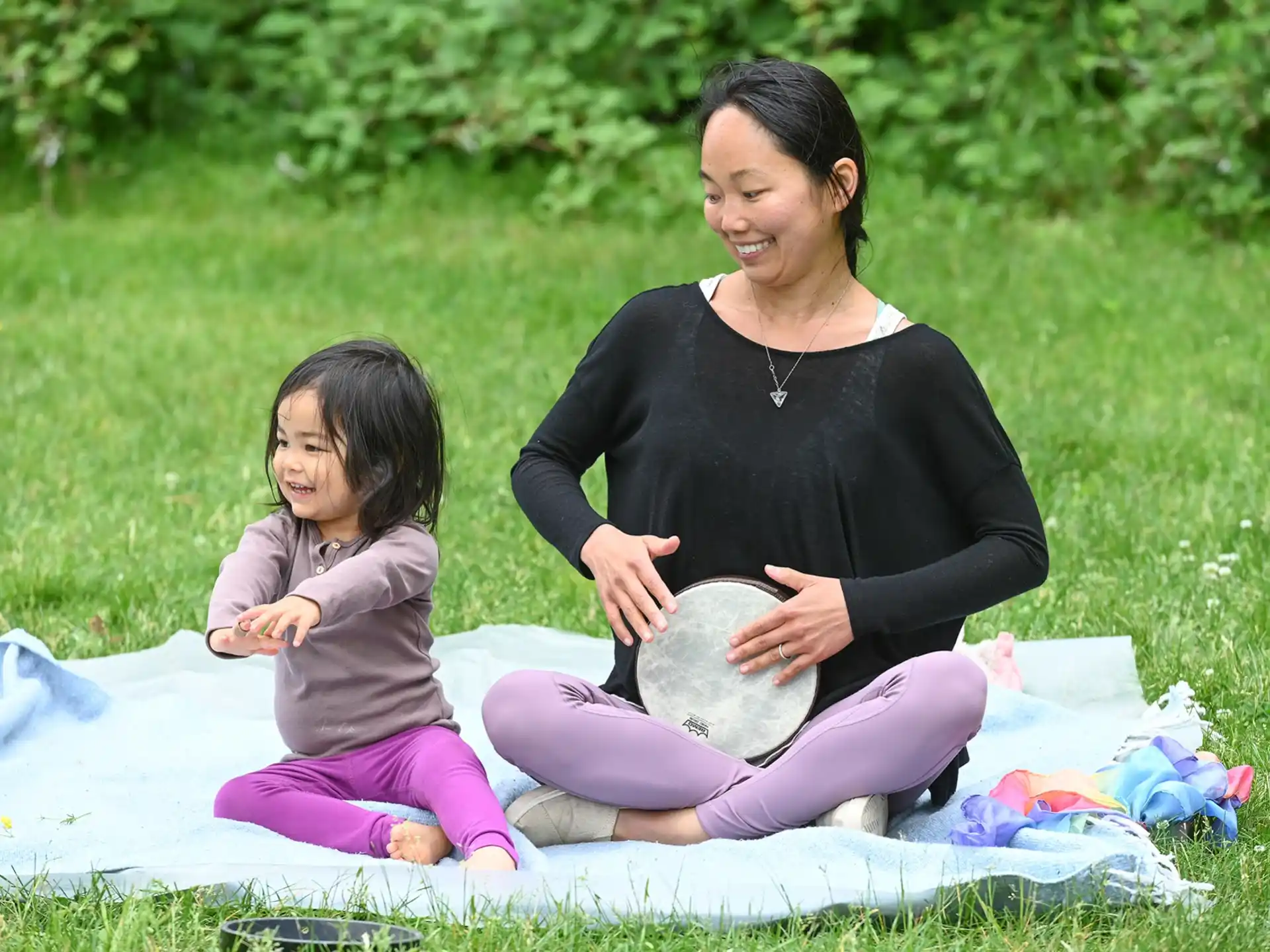 a person and a child sitting on a blanket in the grass