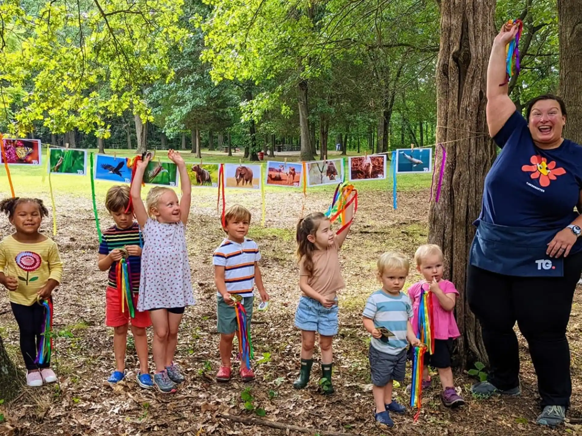 a group of children standing by a tree and a person holding a stick