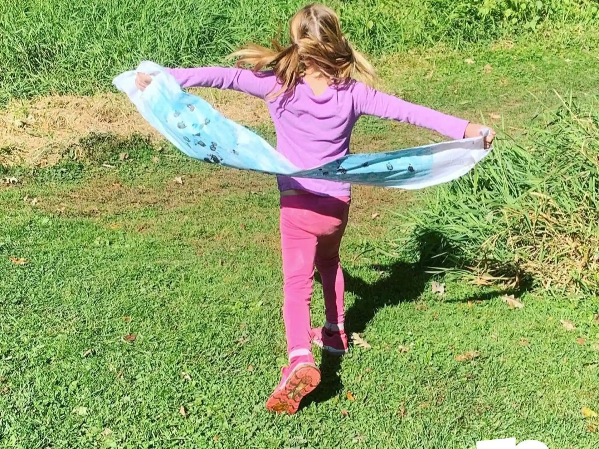 a girl in a purple dress holding a blue and purple tube in a grassy area