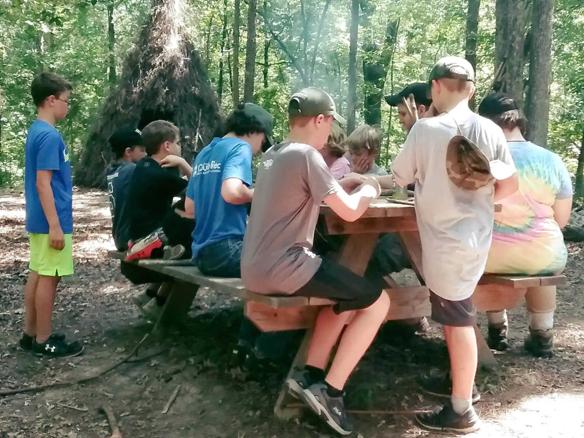 a group of people sitting at a picnic table in the woods