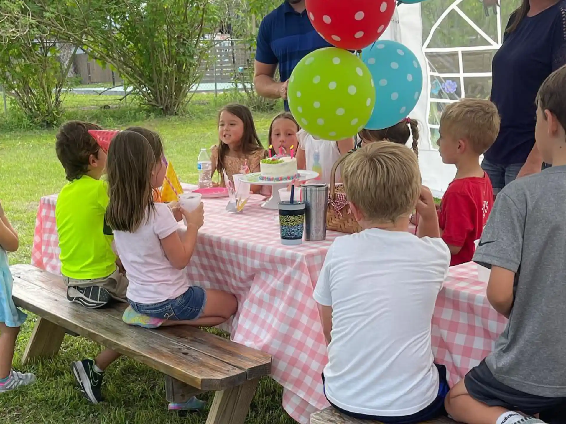 a group of children sitting at a table with food and balloons