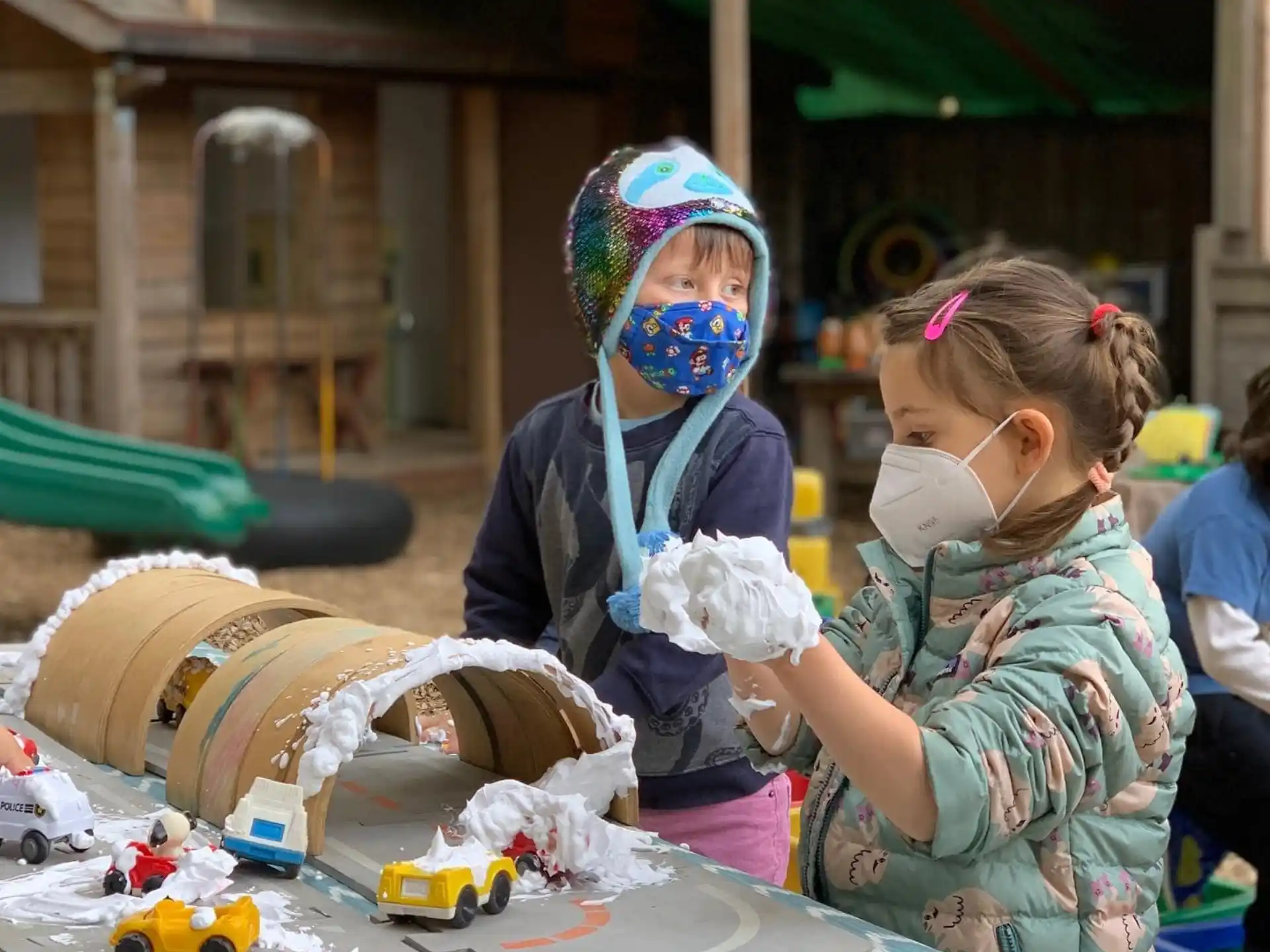 a couple of girls wearing masks and sitting at a table with a robot