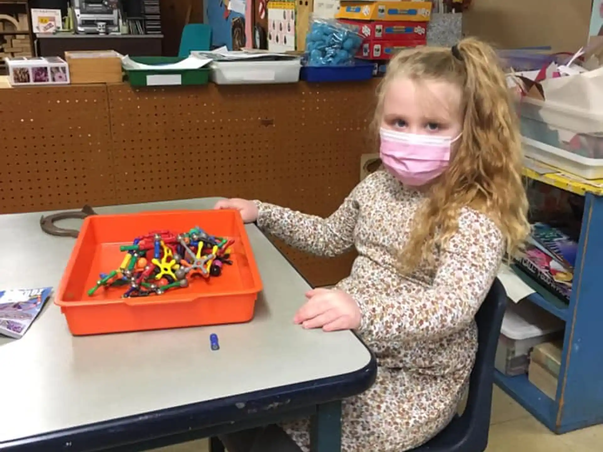 a girl sitting at a table with a toy