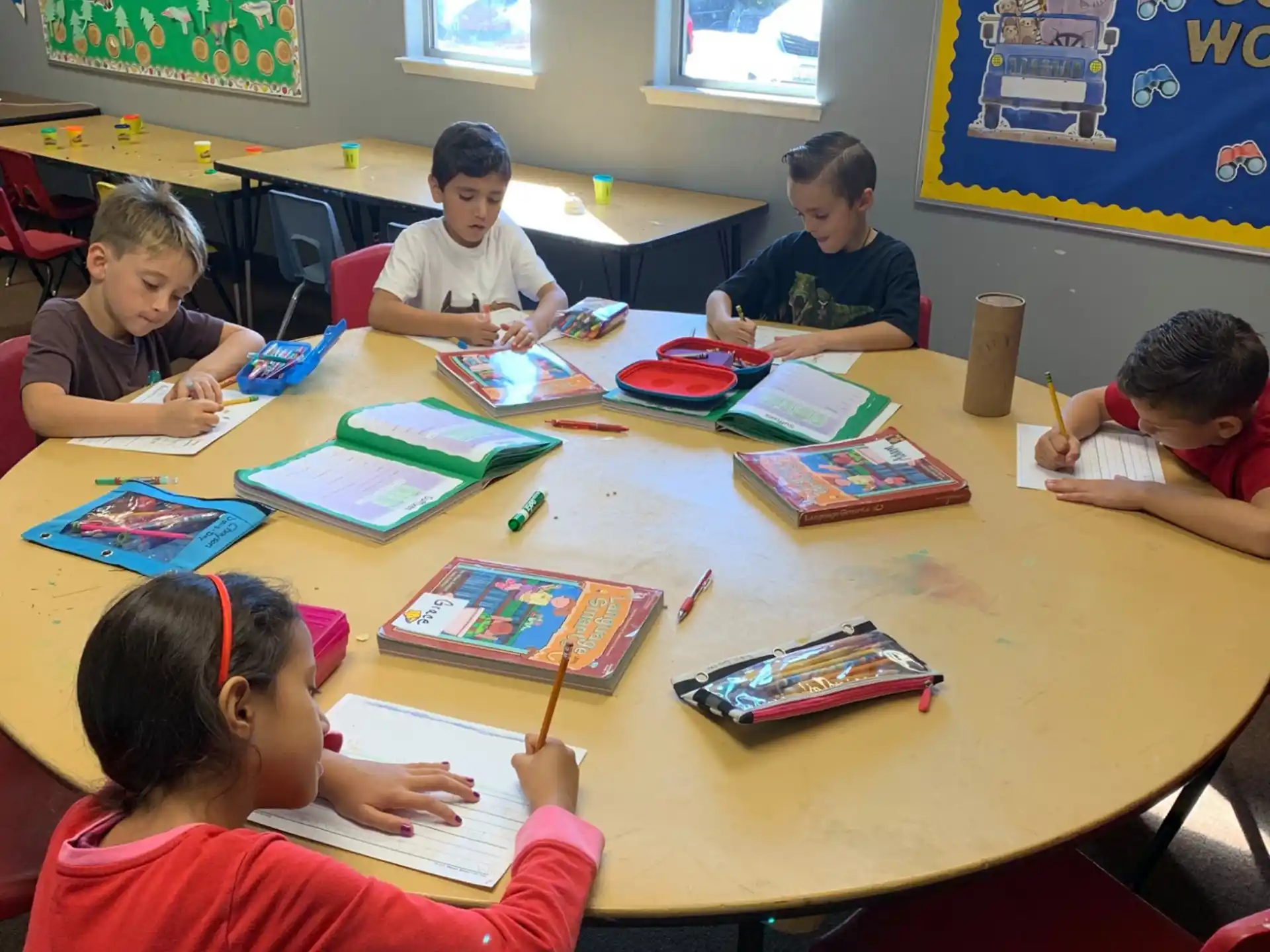 a group of children sitting at a table with books and pencils