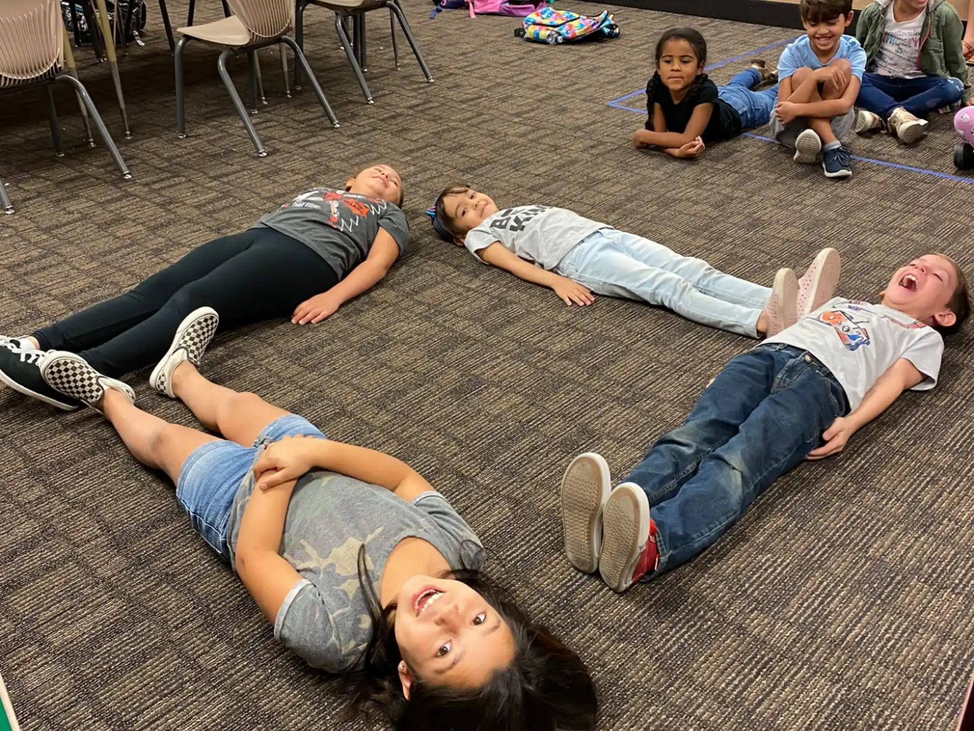 a group of people lying on the floor in a room with tables and chairs
